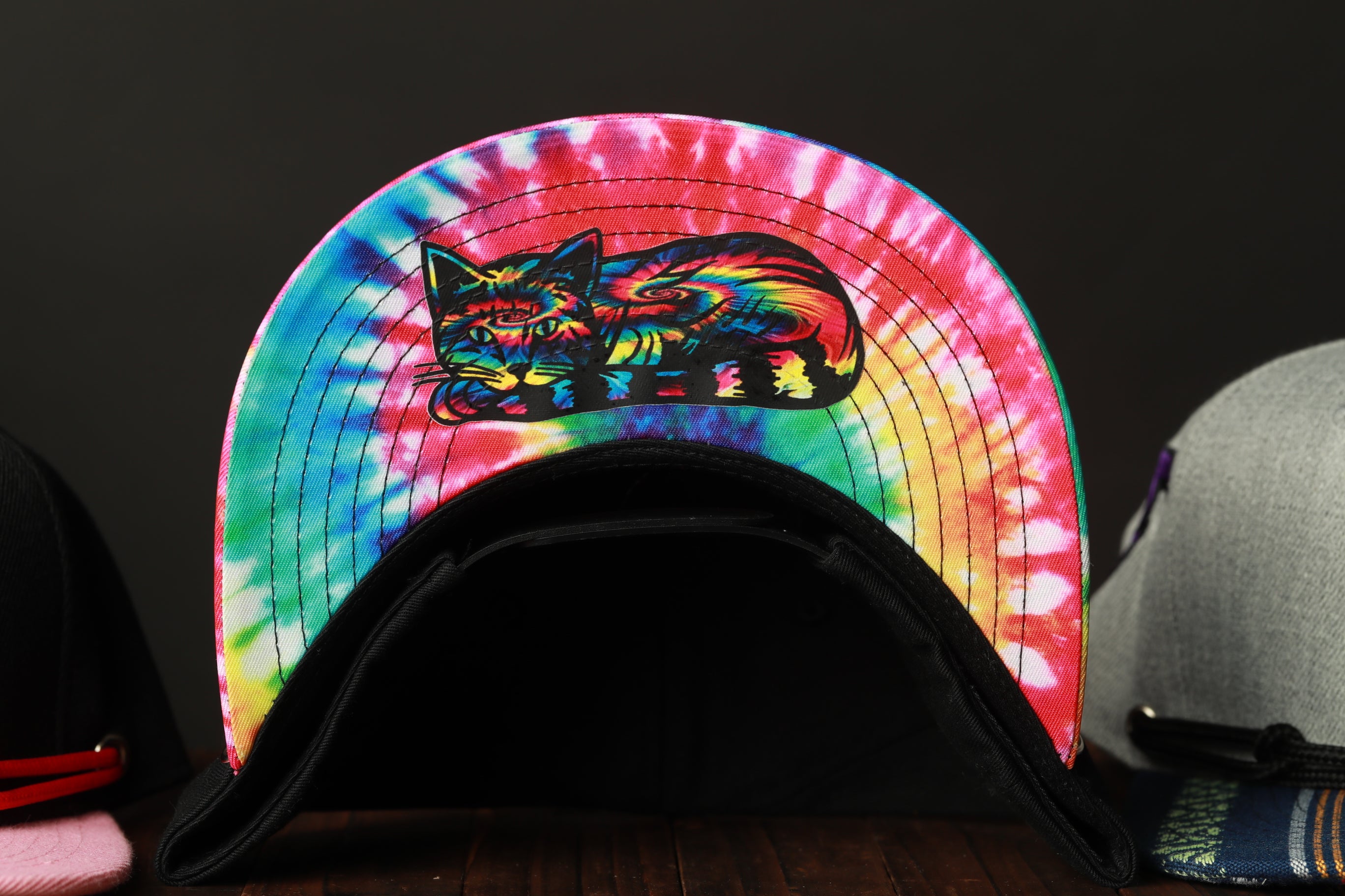 A tie-dye baseball cap with a colorful cat design on the front.