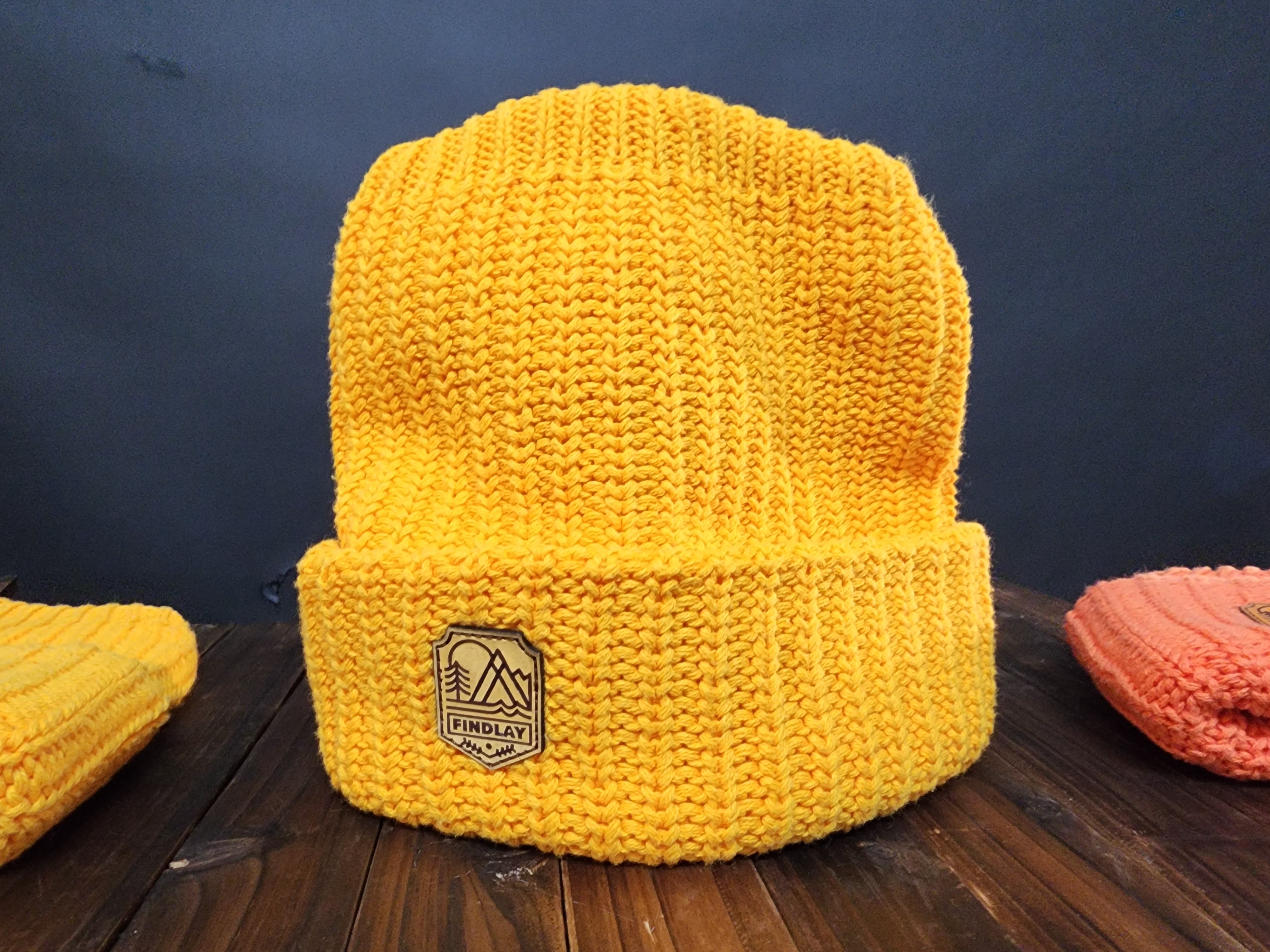 A bright yellow knit beanie with a mountain-like logo on the front, sitting on a wooden surface.