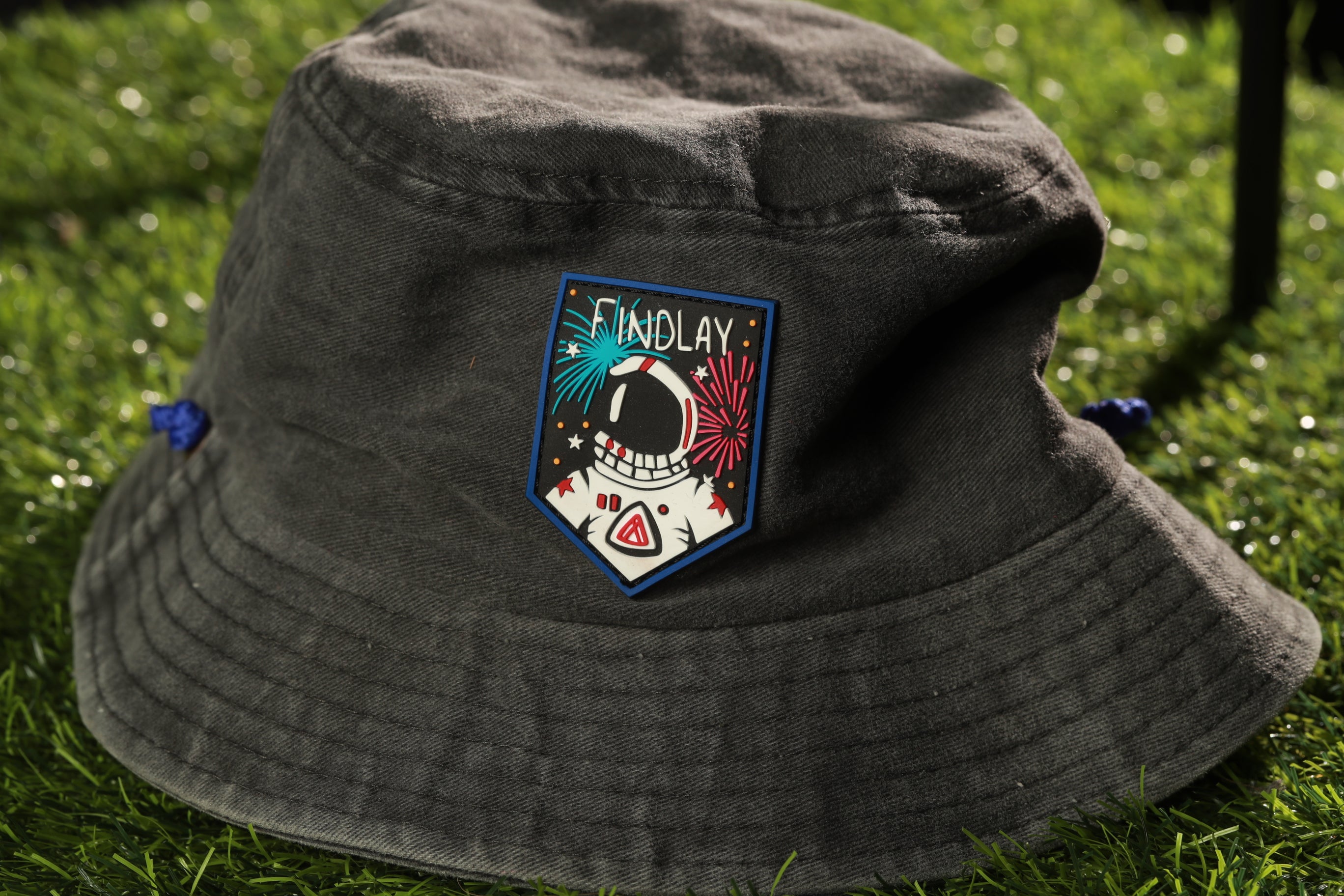 A gray bucket hat with a patch featuring an astronaut and colorful fireworks.