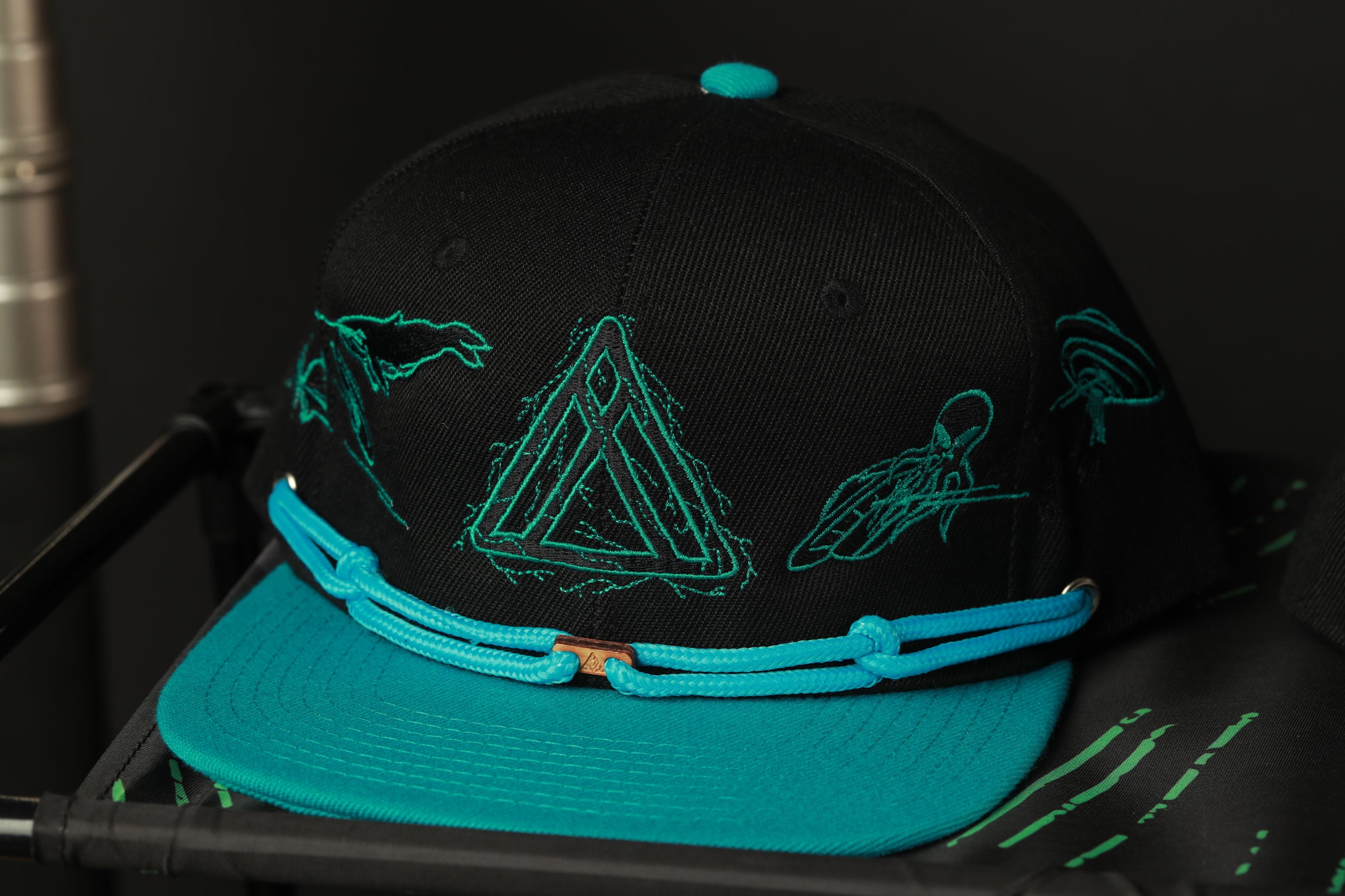 A black baseball cap with teal accents and a geometric design on the front.