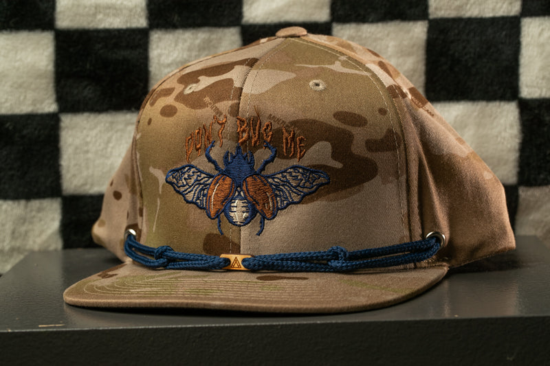 A camouflage baseball cap with a blue and orange insect design and the text "Don't Bug Me" printed on it.