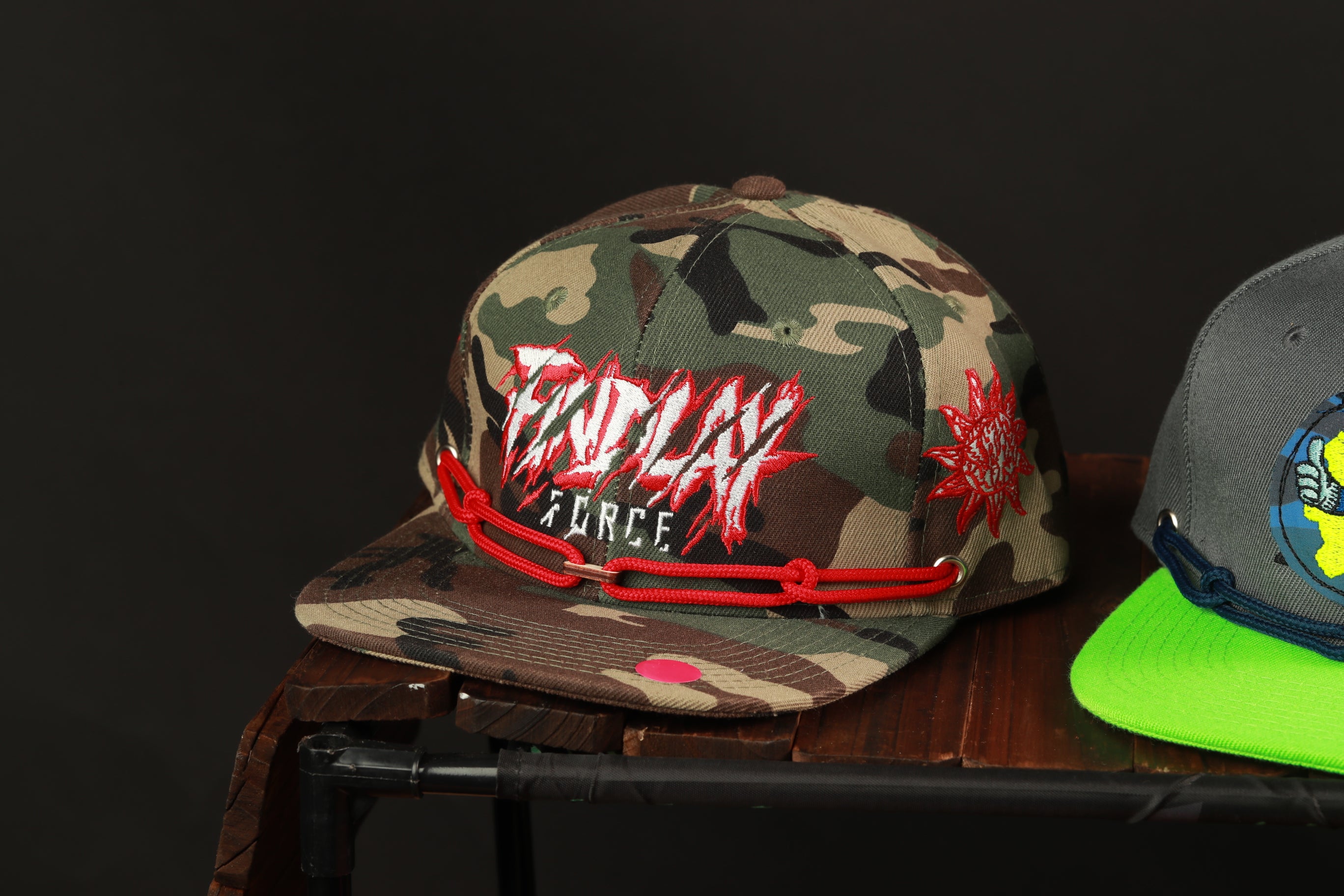 A camouflage baseball cap with the text "ENDPLAY FORCE" printed on it, along with a red chain strap.
