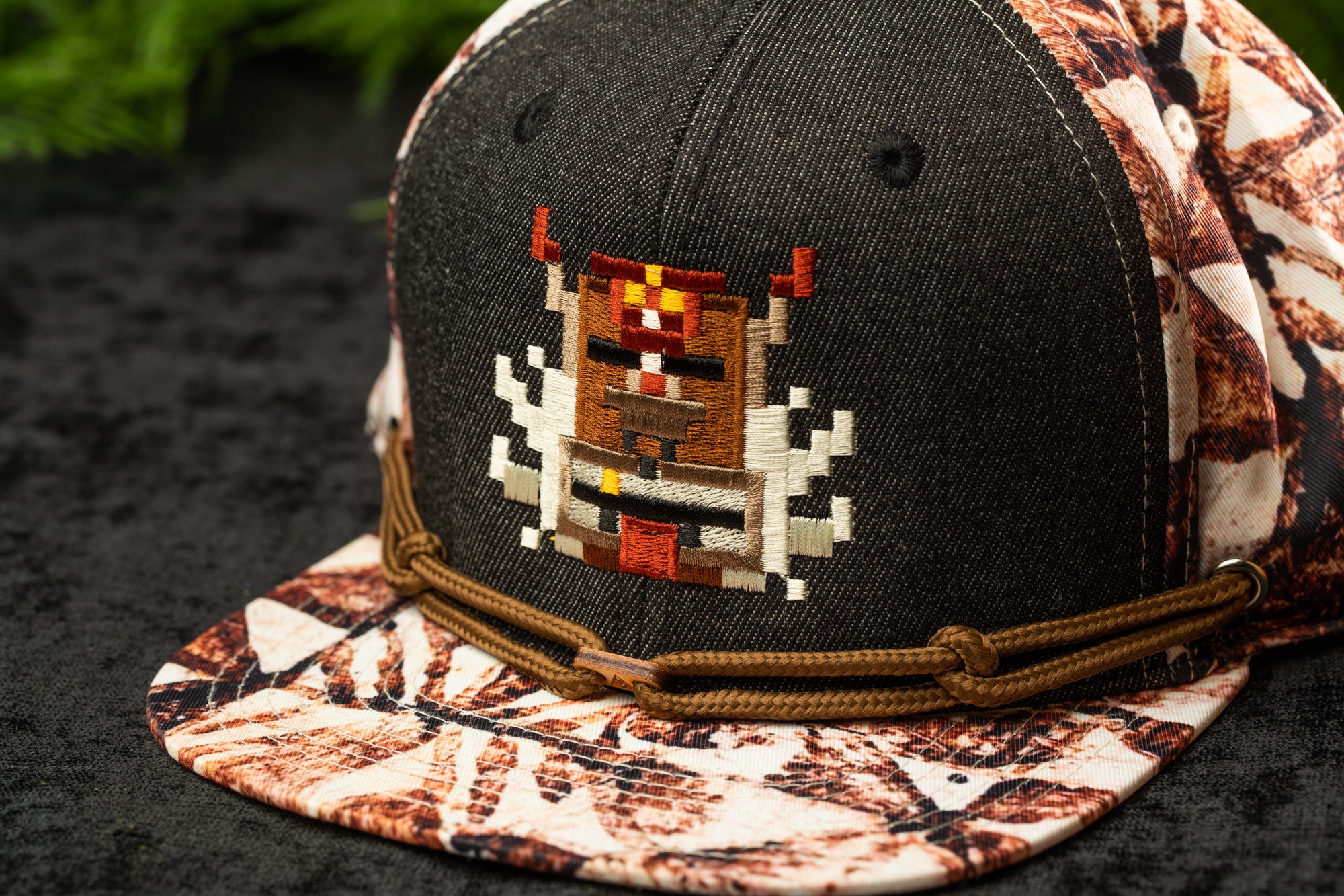 A close-up image of a black baseball cap with a colorful, pixelated design on the front.
