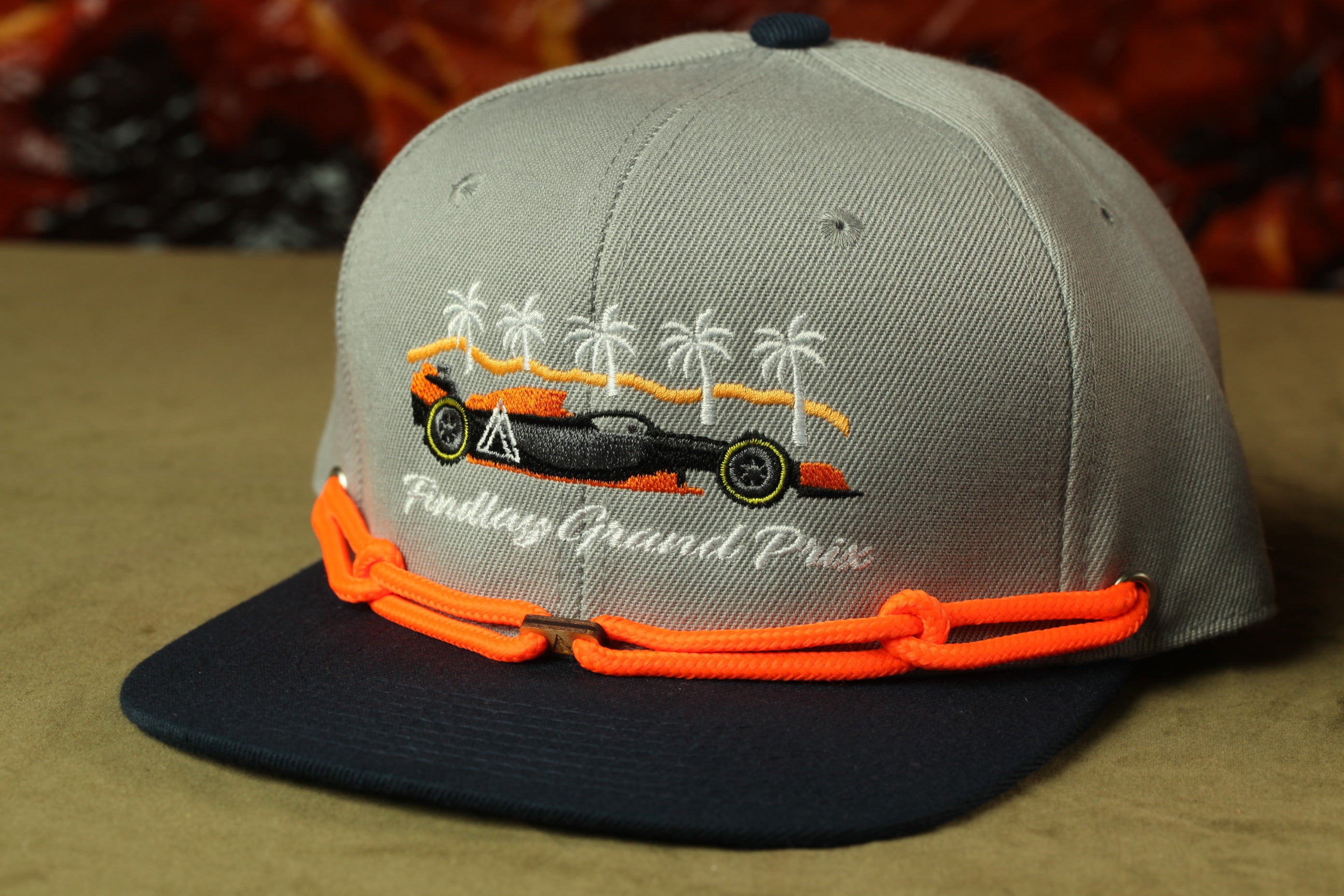 A grey baseball cap with an embroidered design of a race car and palm trees, along with the text "Findlay Grand Prix".