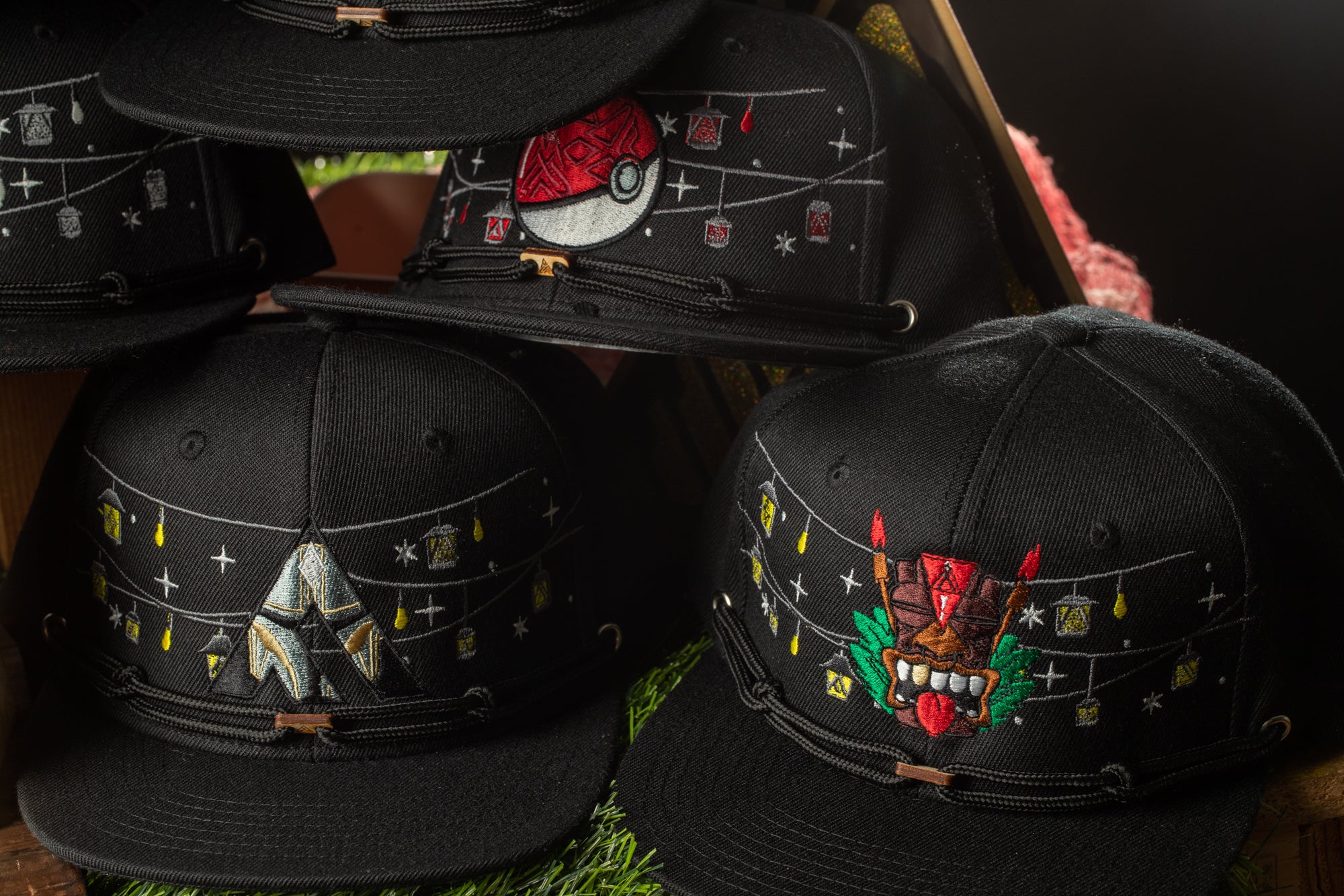 A collection of black baseball caps with various designs and patterns, including a red and white Pokemon character, a black mask, and other decorative elements.
