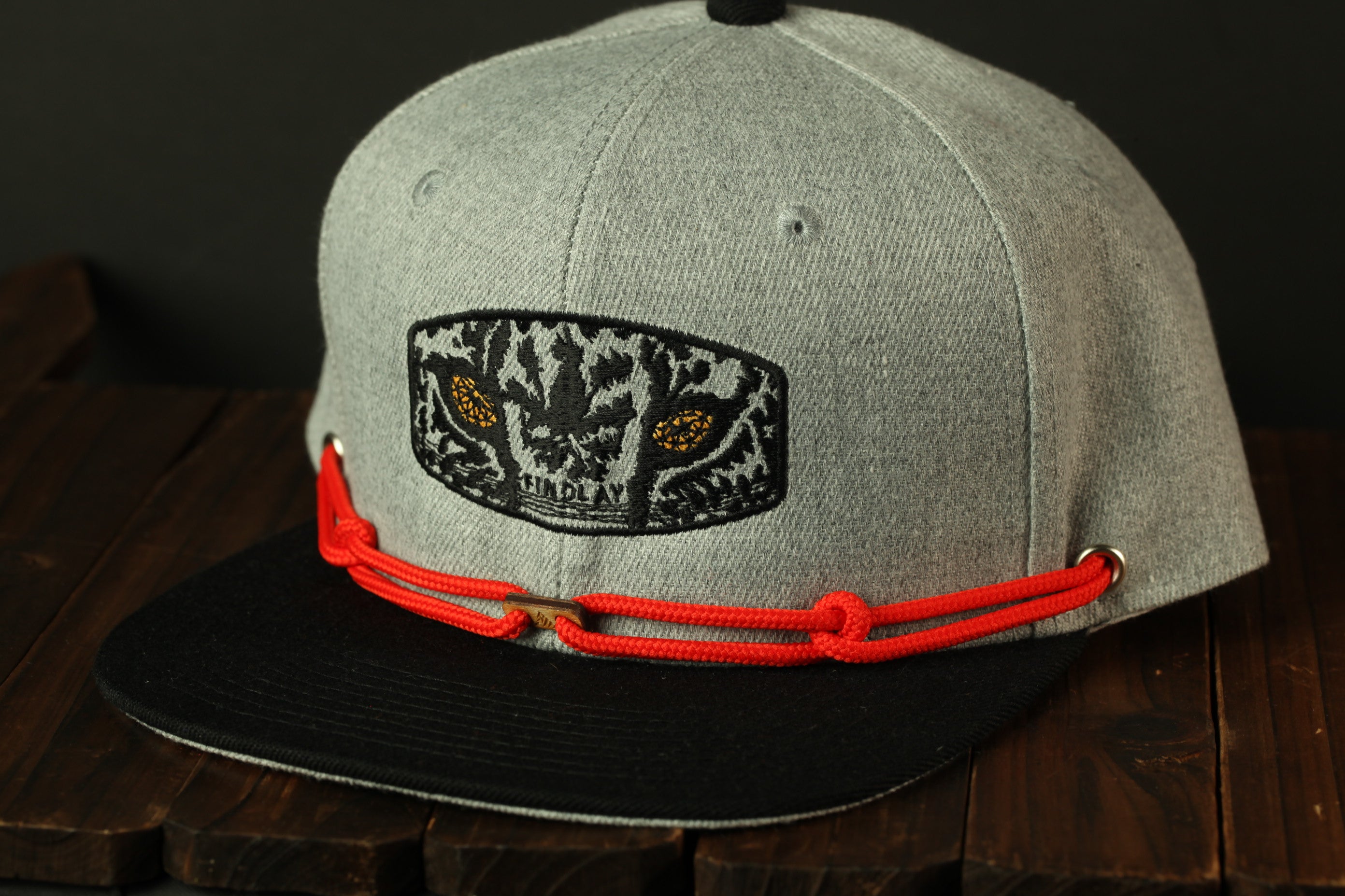 A gray baseball cap with a black and red braided strap, featuring a tiger-like design on the front.