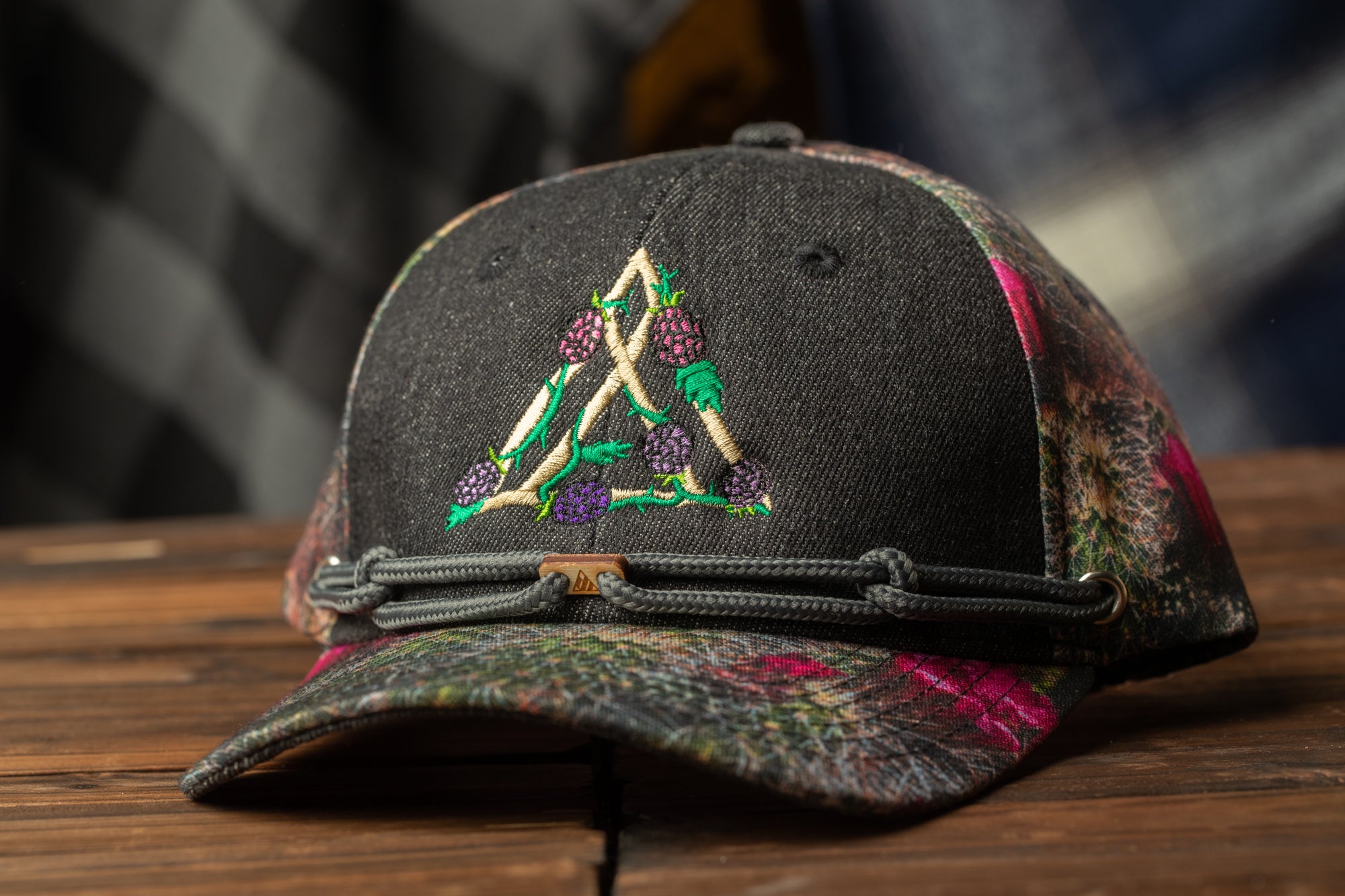 A black baseball cap with a floral pattern and a small triangle design on the front, resting on a wooden surface.