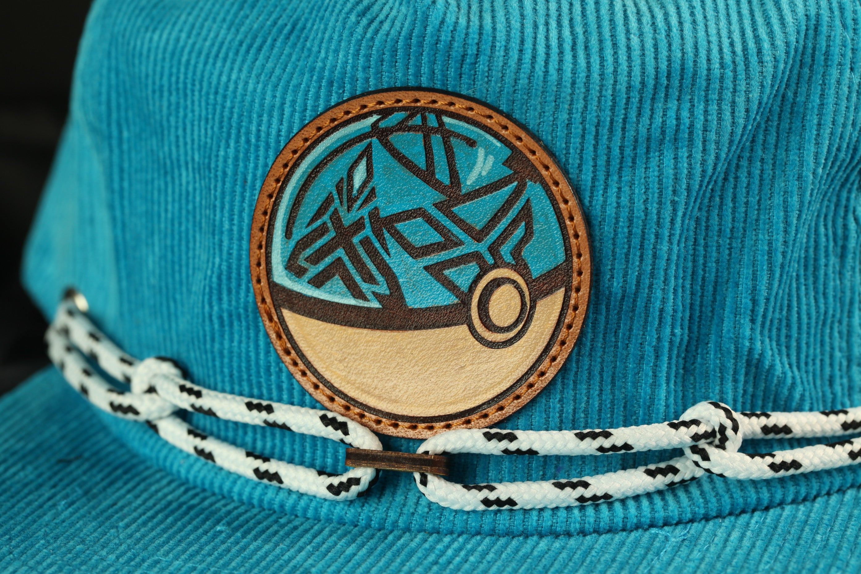 A close-up view of a turquoise-colored hat with a circular patch featuring a geometric design and a small circular element.