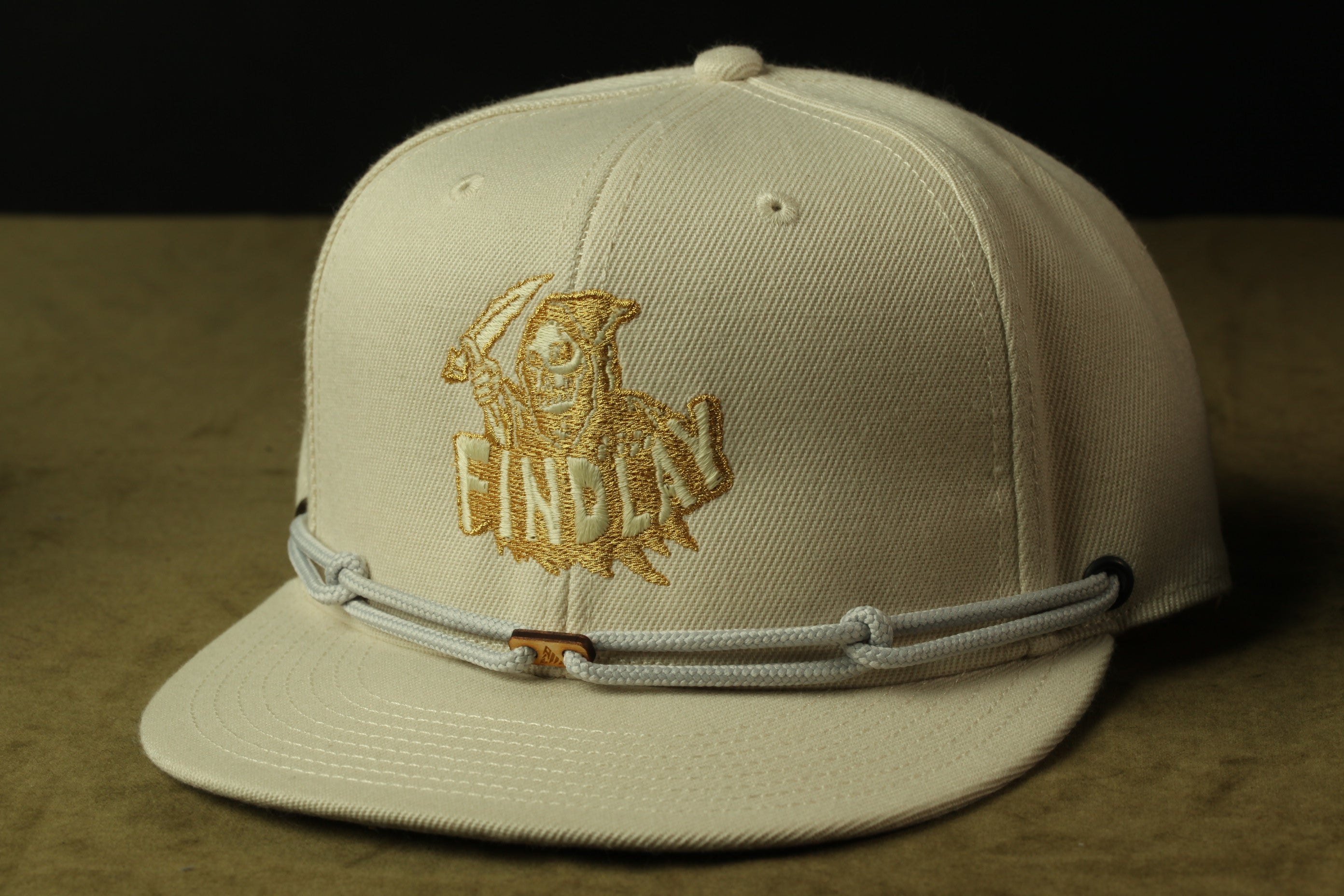 A beige baseball cap with a gold embroidered logo on the front.