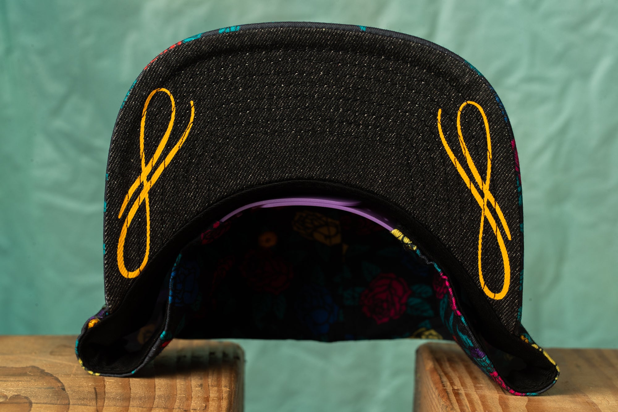 A black baseball cap with yellow embroidered designs on the brim and a colorful floral pattern inside the brim.