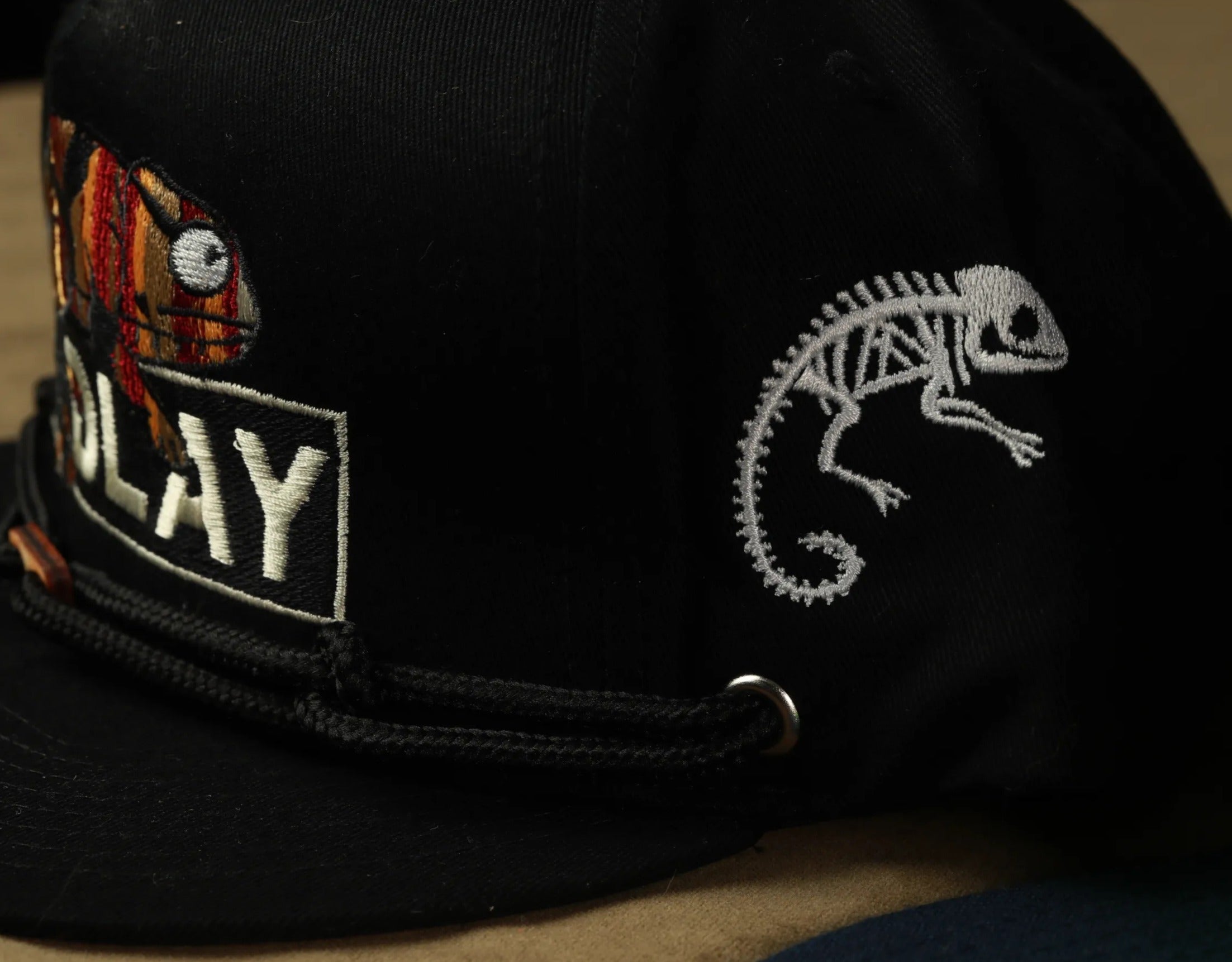 A close-up view of a black baseball cap with a chameleon design on the side.