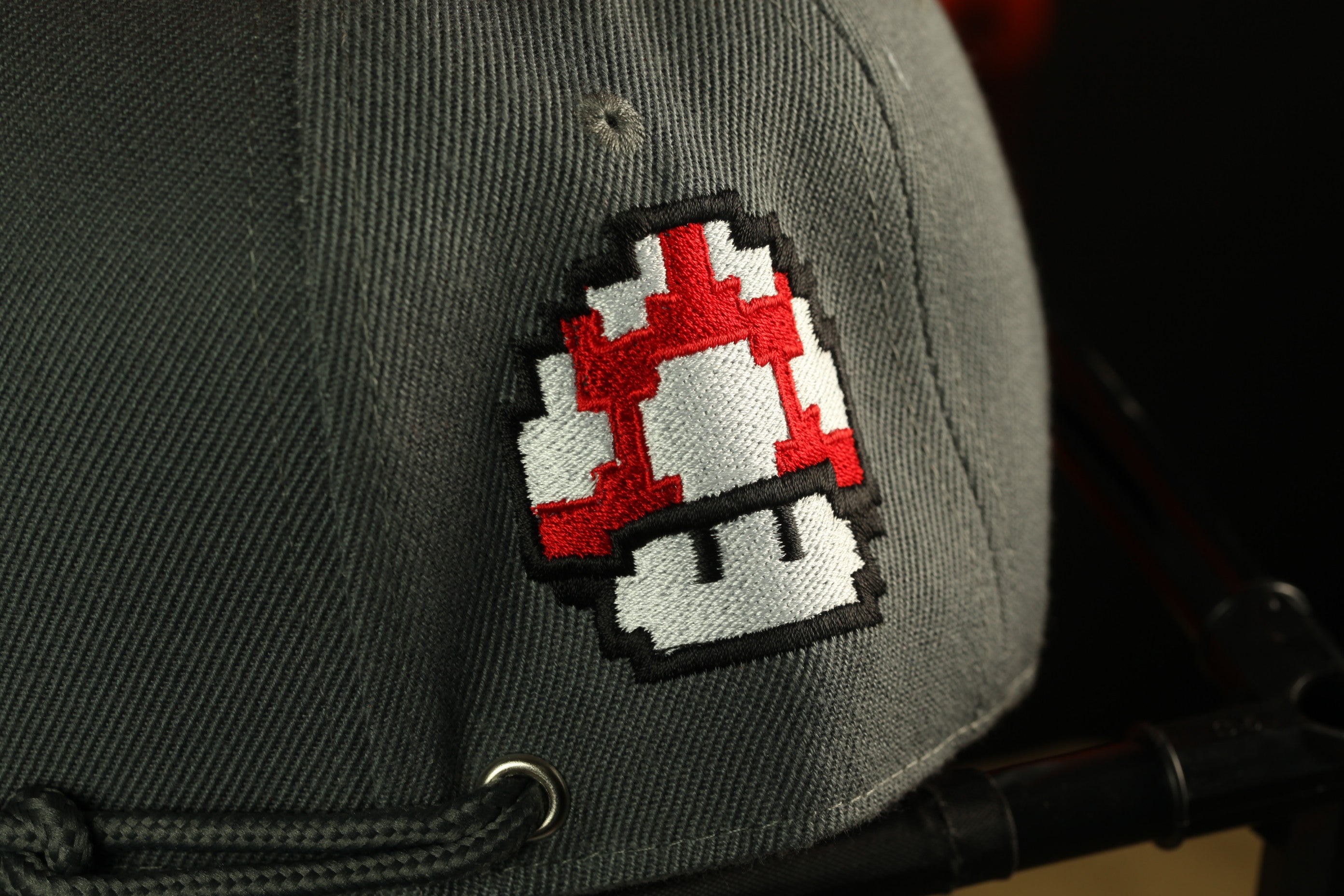 a gray baseball cap with a red and white mushroom-shaped embroidered patch on the front.