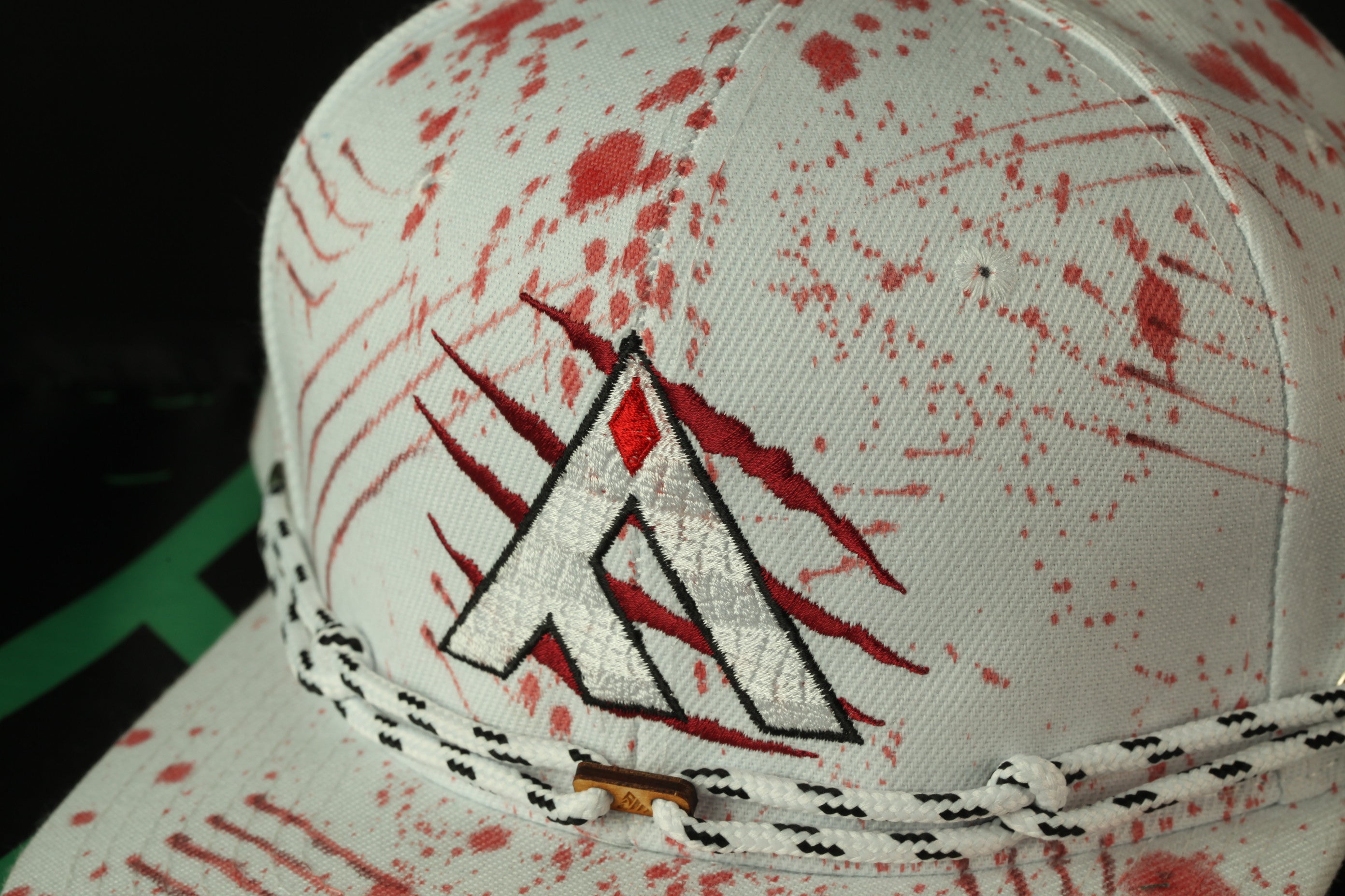 A close-up view of a white baseball cap with a red splatter pattern and a black and white braided strap.