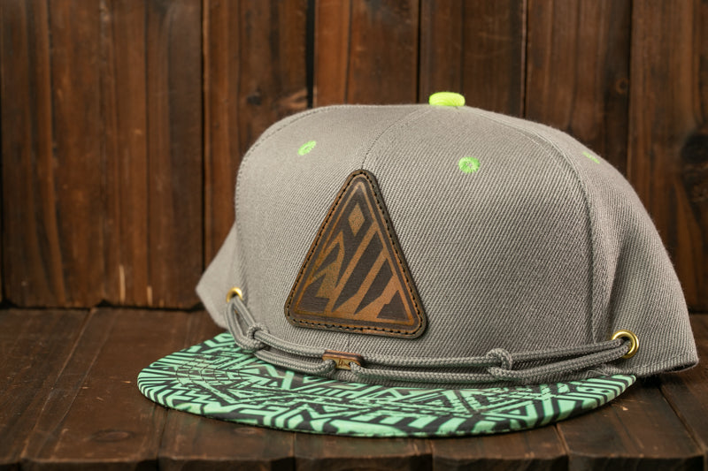 A gray baseball cap with a green and black geometric pattern on the front, placed on a wooden surface.