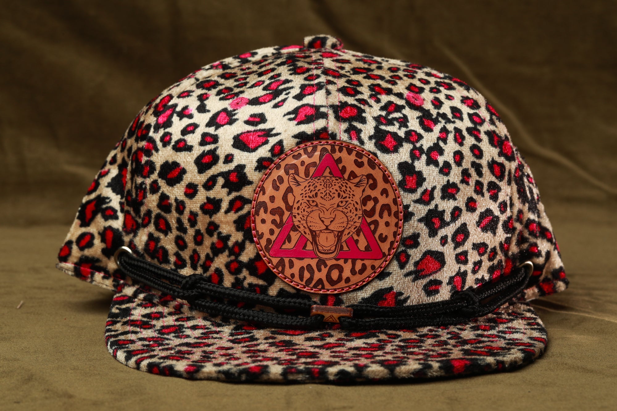 A leopard print baseball cap with a leather patch featuring a stylized leopard face.