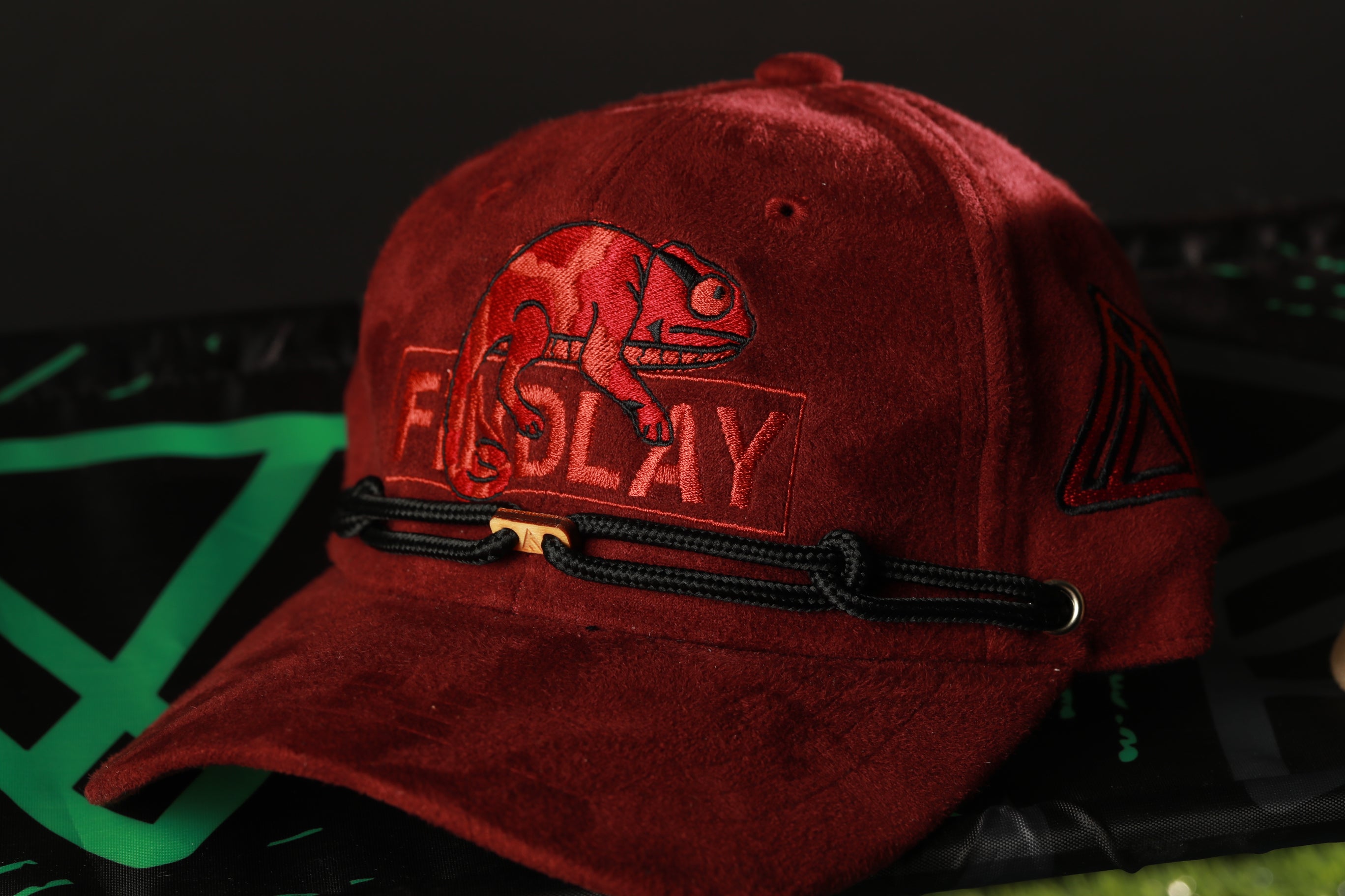 A red baseball cap with a red chameleon design and the word "FIRST" printed on it.