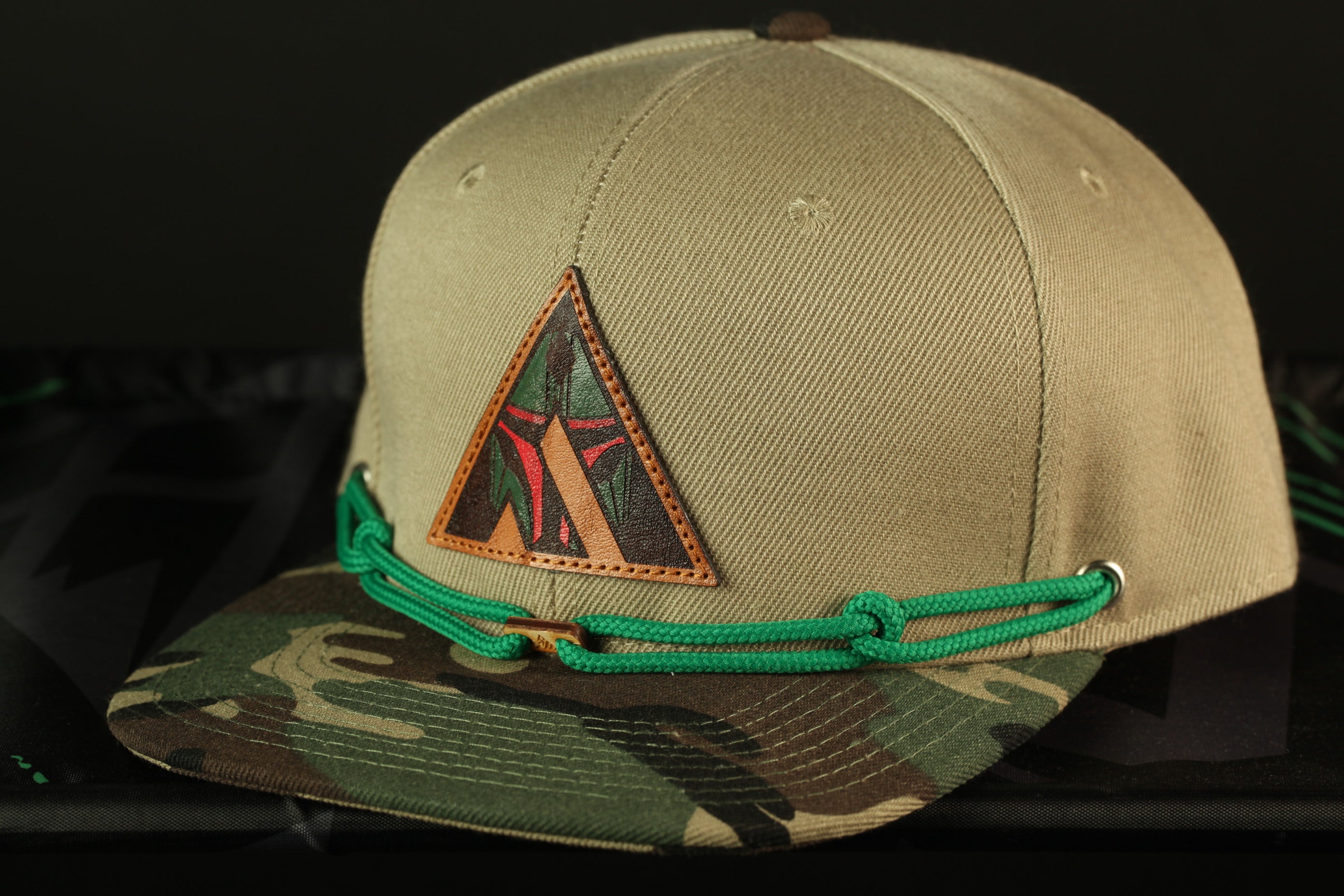 A beige baseball cap with a camouflage pattern and a triangular patch on the front.