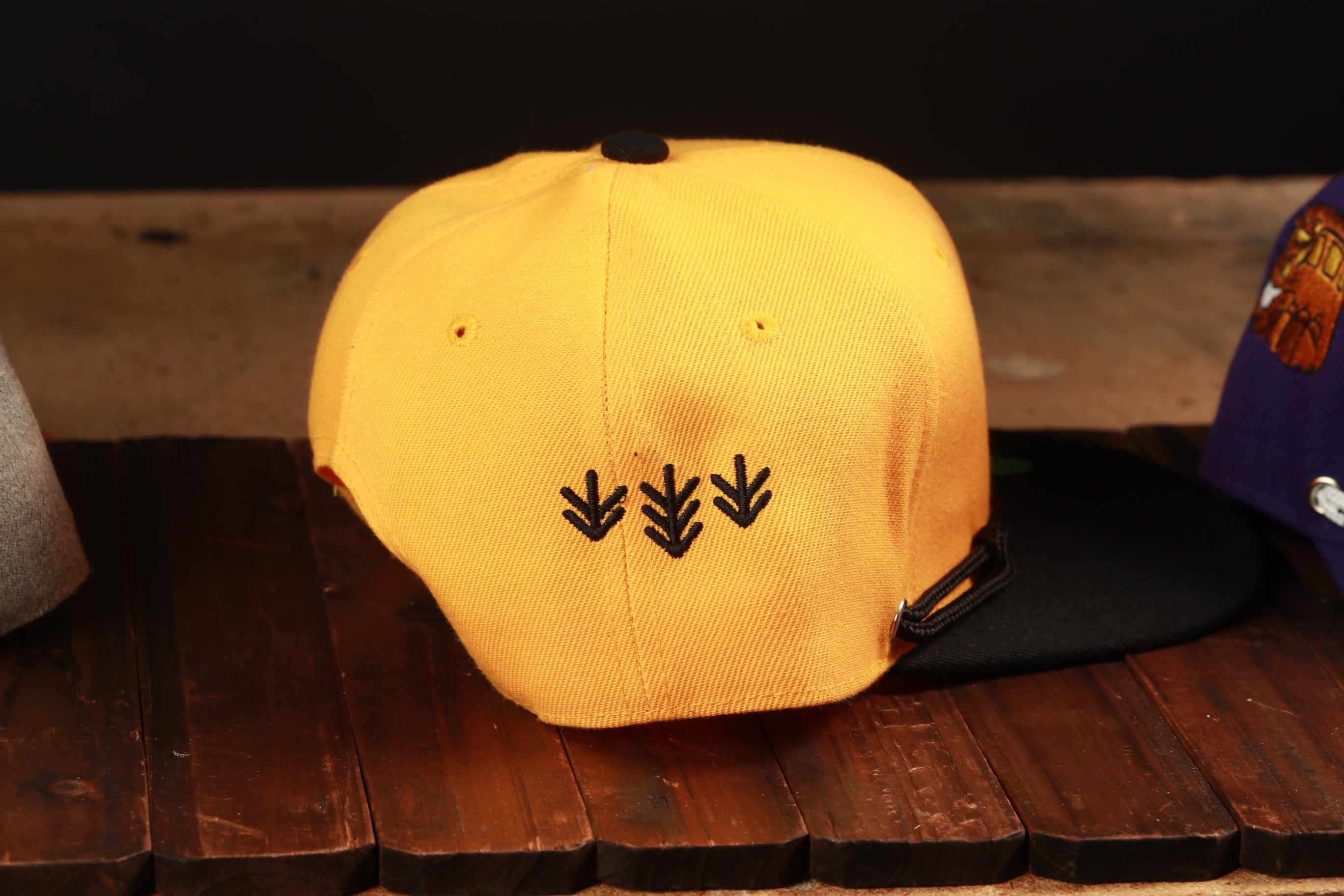 A yellow baseball cap with black embroidered designs on the front, placed on a wooden surface.