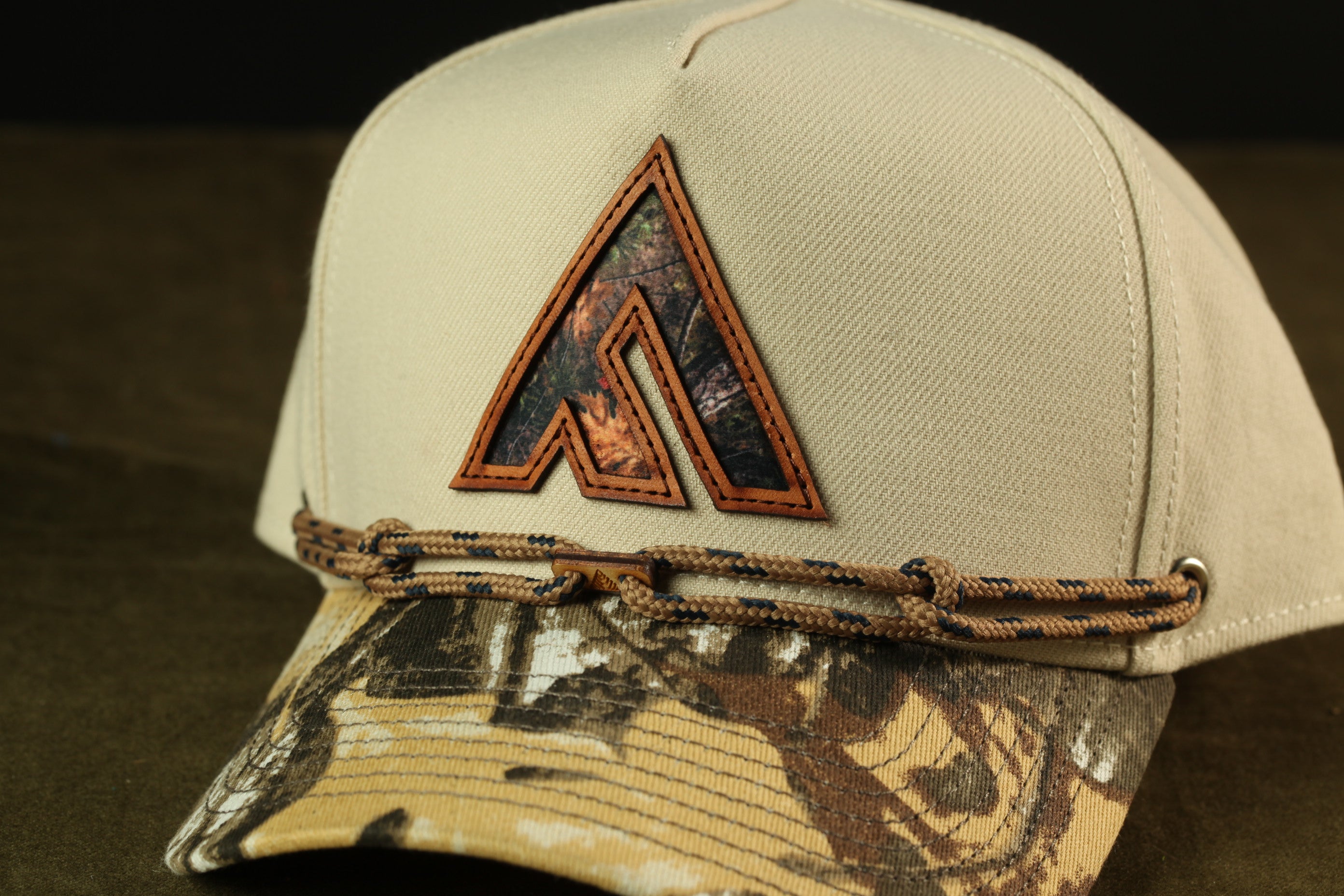 A beige baseball cap with a camouflage pattern and a logo on the front.