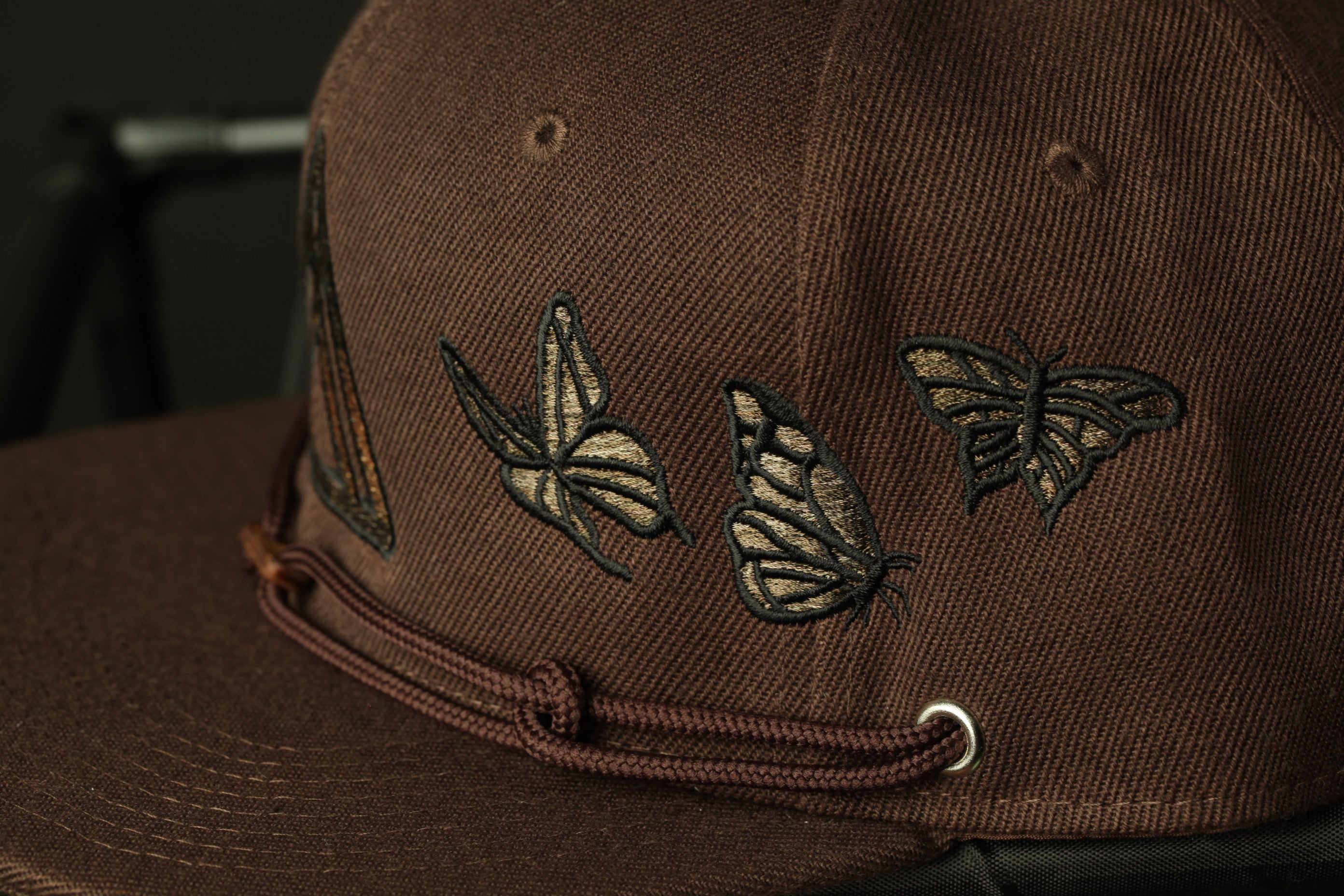 A close-up view of a brown baseball cap with a design of butterflies on the front.