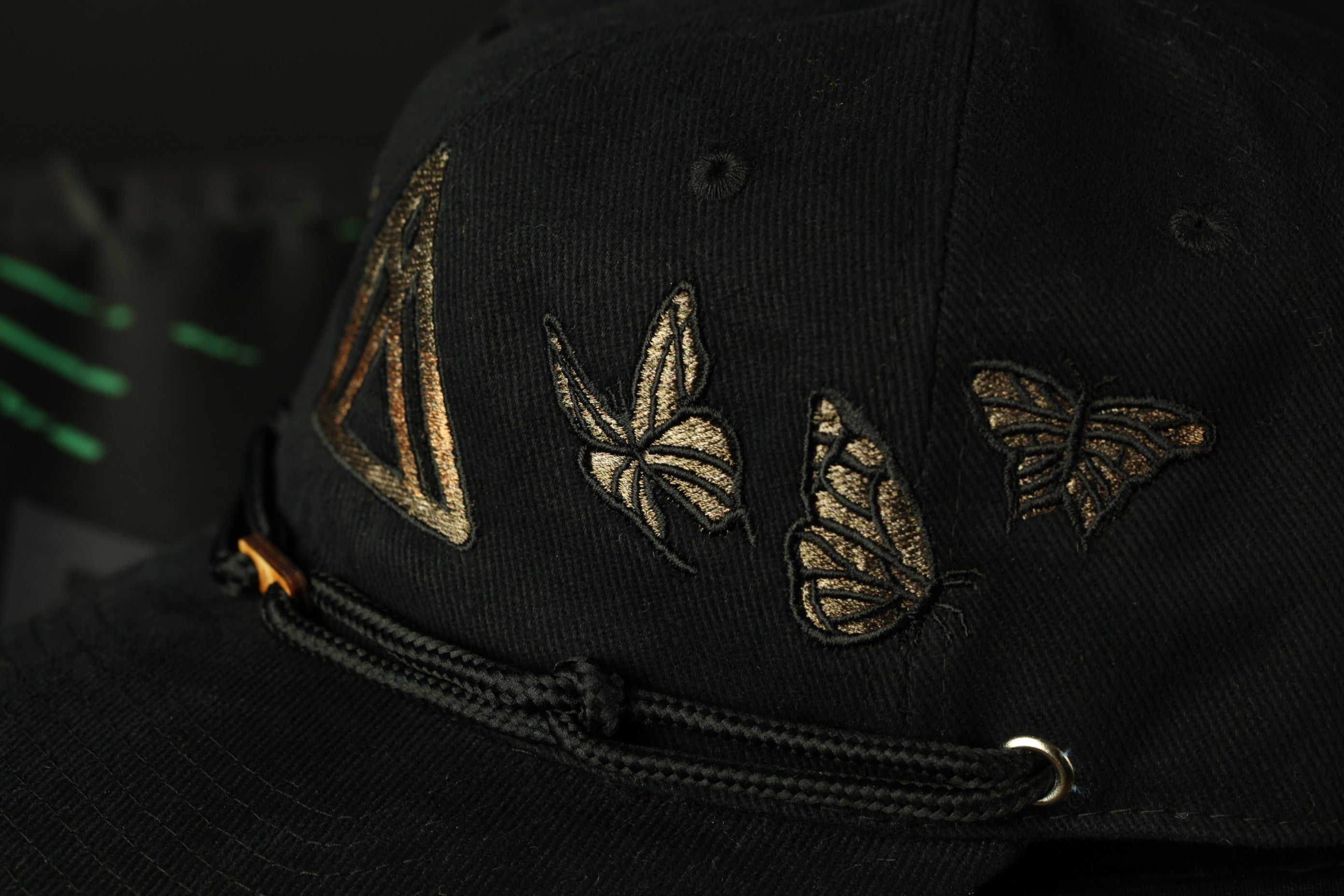 A close-up view of a black baseball cap with gold butterfly and triangle designs on the front.