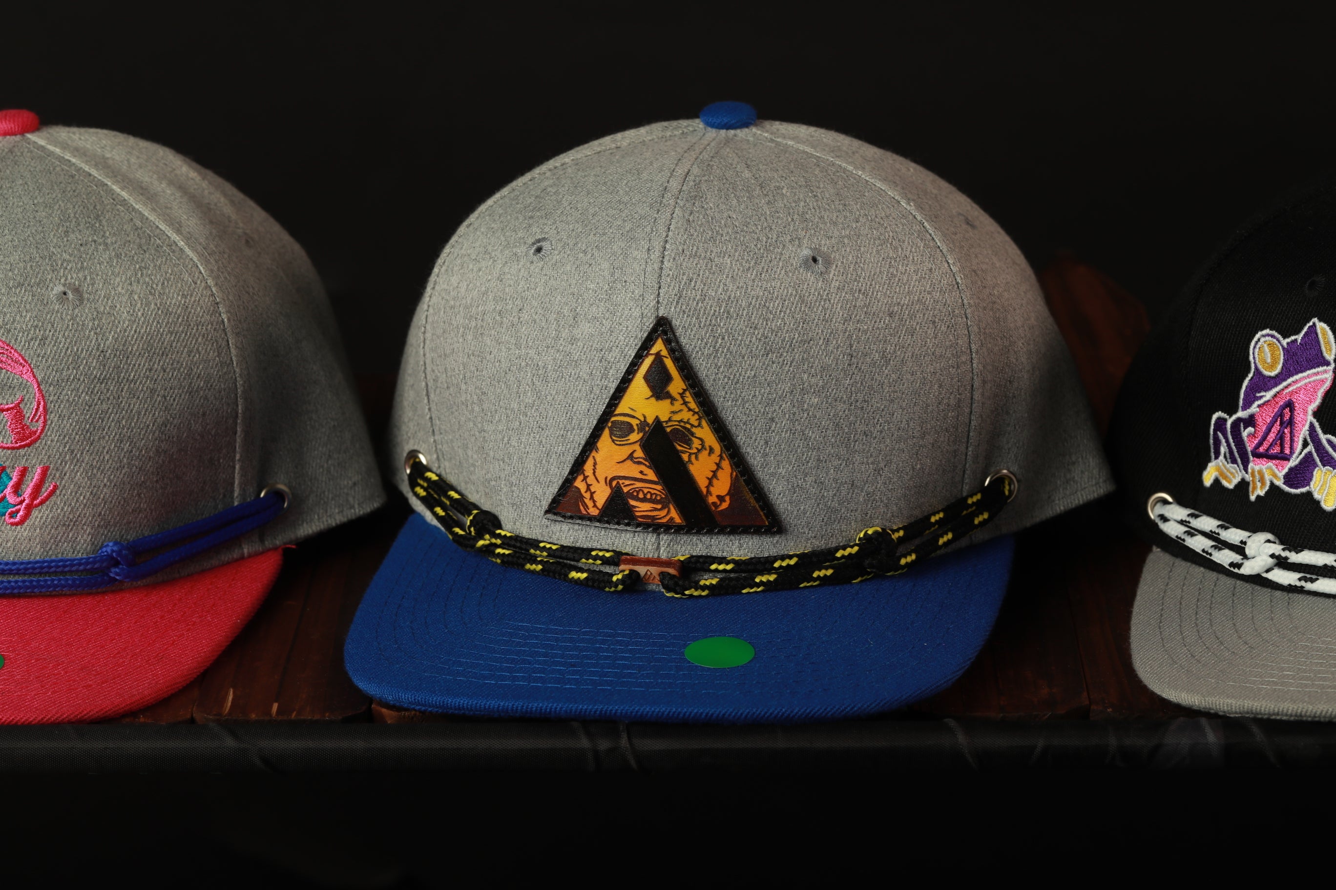 Three baseball caps are displayed on a shelf, each with different colors and designs.