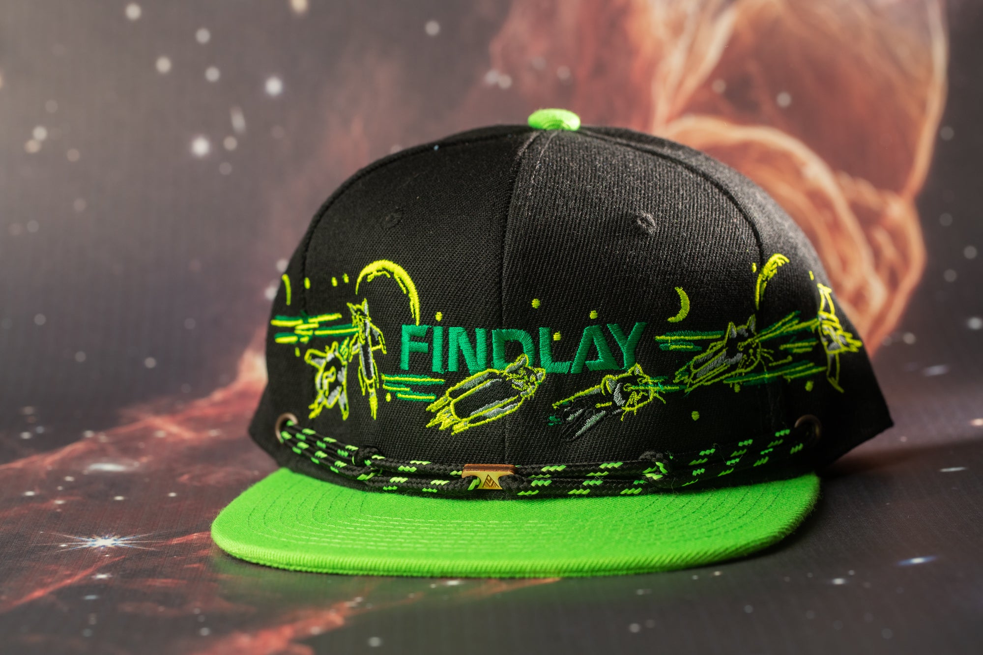 A black baseball cap with green accents, featuring the word "FINDlay" printed on it, is displayed against a dark background with stars.