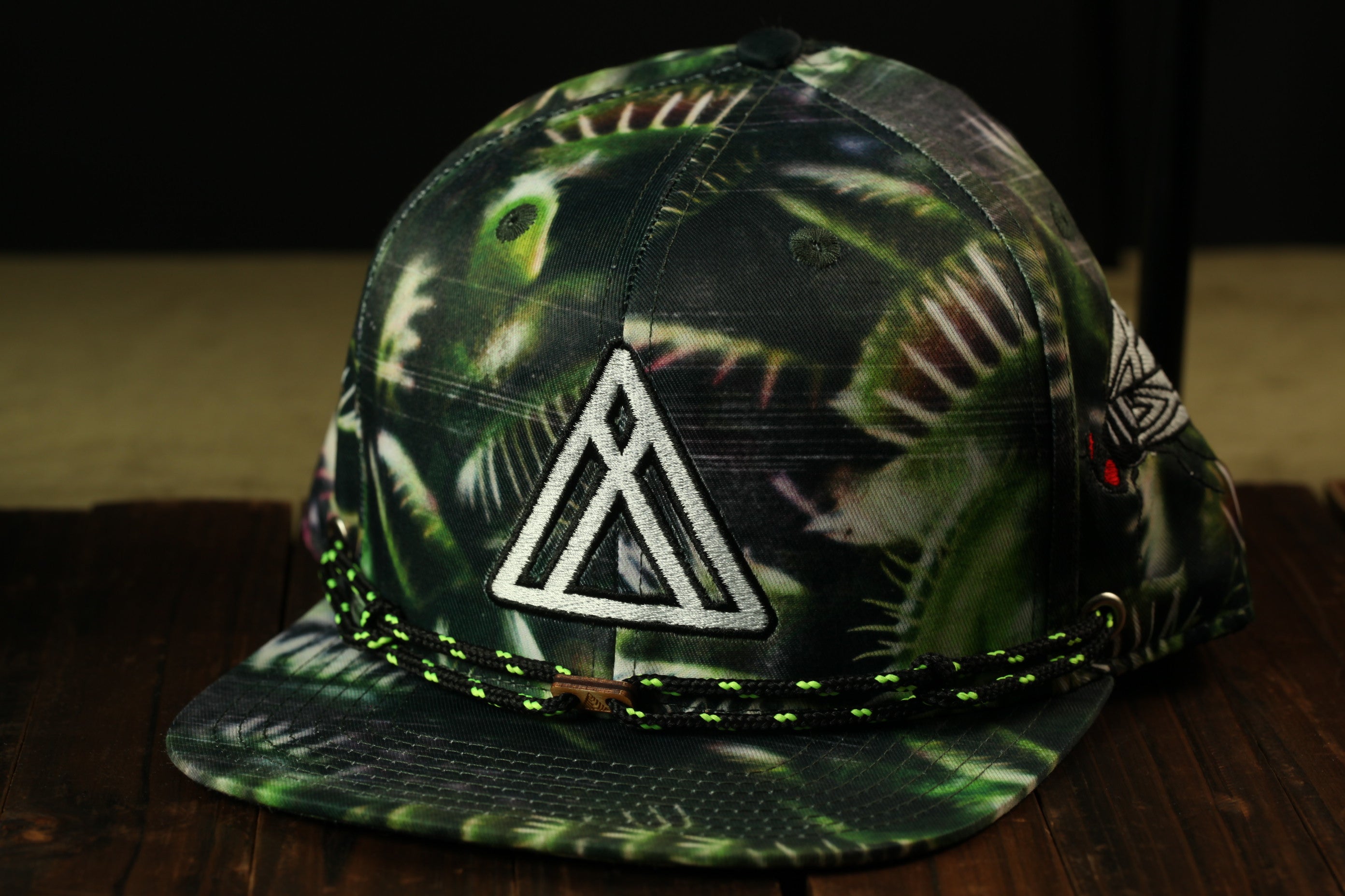 A camouflage-patterned baseball cap with a white triangle logo on the front, sitting on a wooden surface.