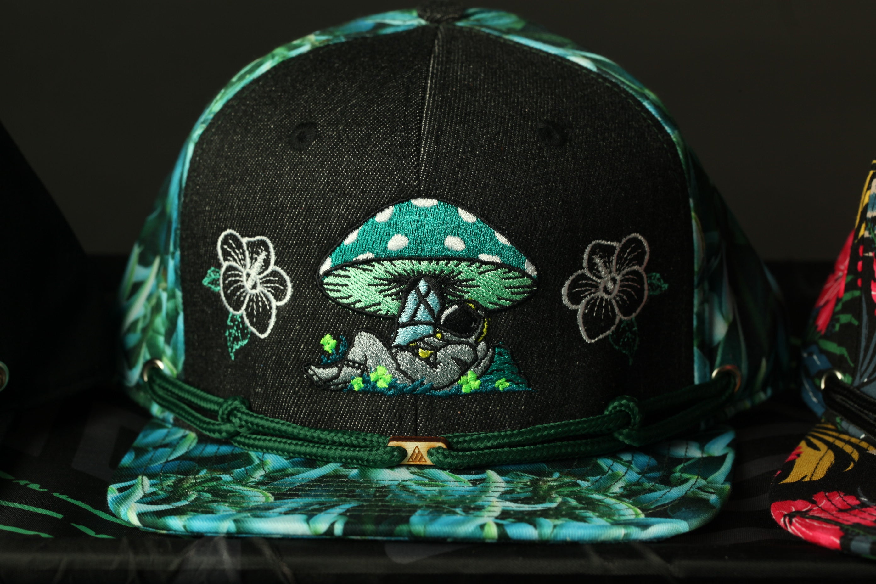 A black baseball cap with a colorful, floral-patterned design featuring a mushroom and flowers.