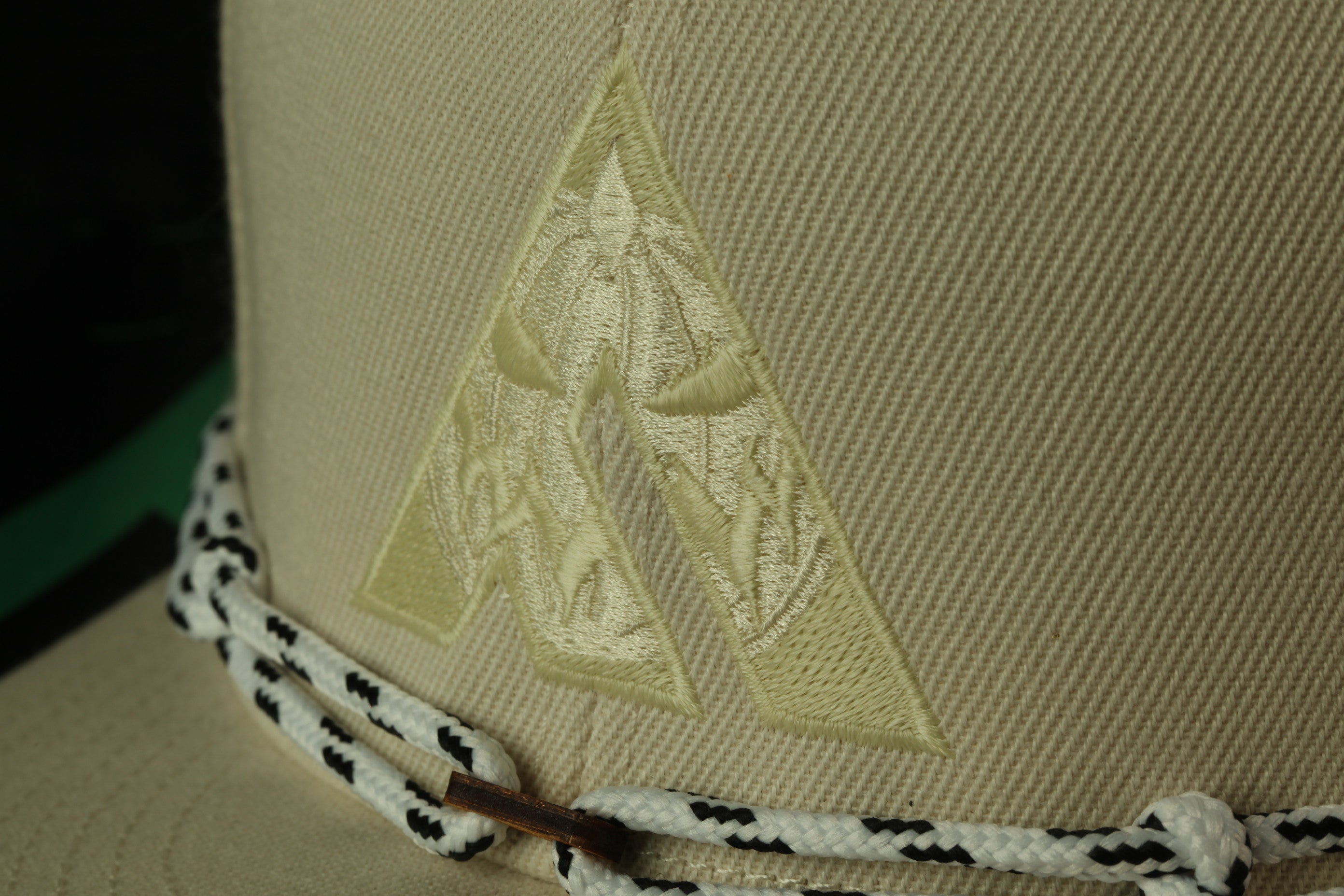 A close-up view of a beige fabric with a yellow triangle-shaped embroidered design on it, along with a black and white rope or belt.