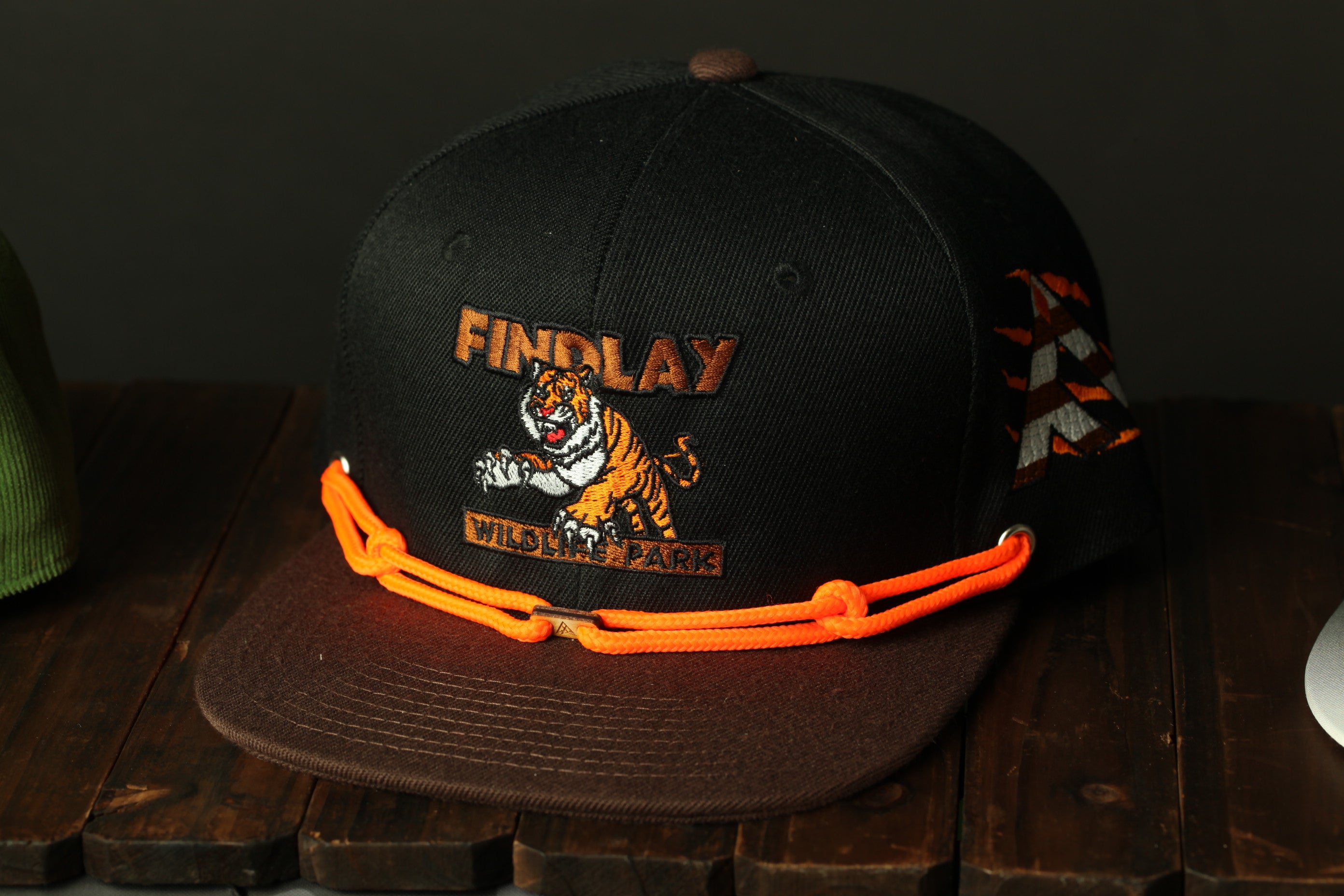 A black baseball cap with orange straps, featuring a tiger graphic and the text "FINDlay WILD LIFE PARK" printed on it.