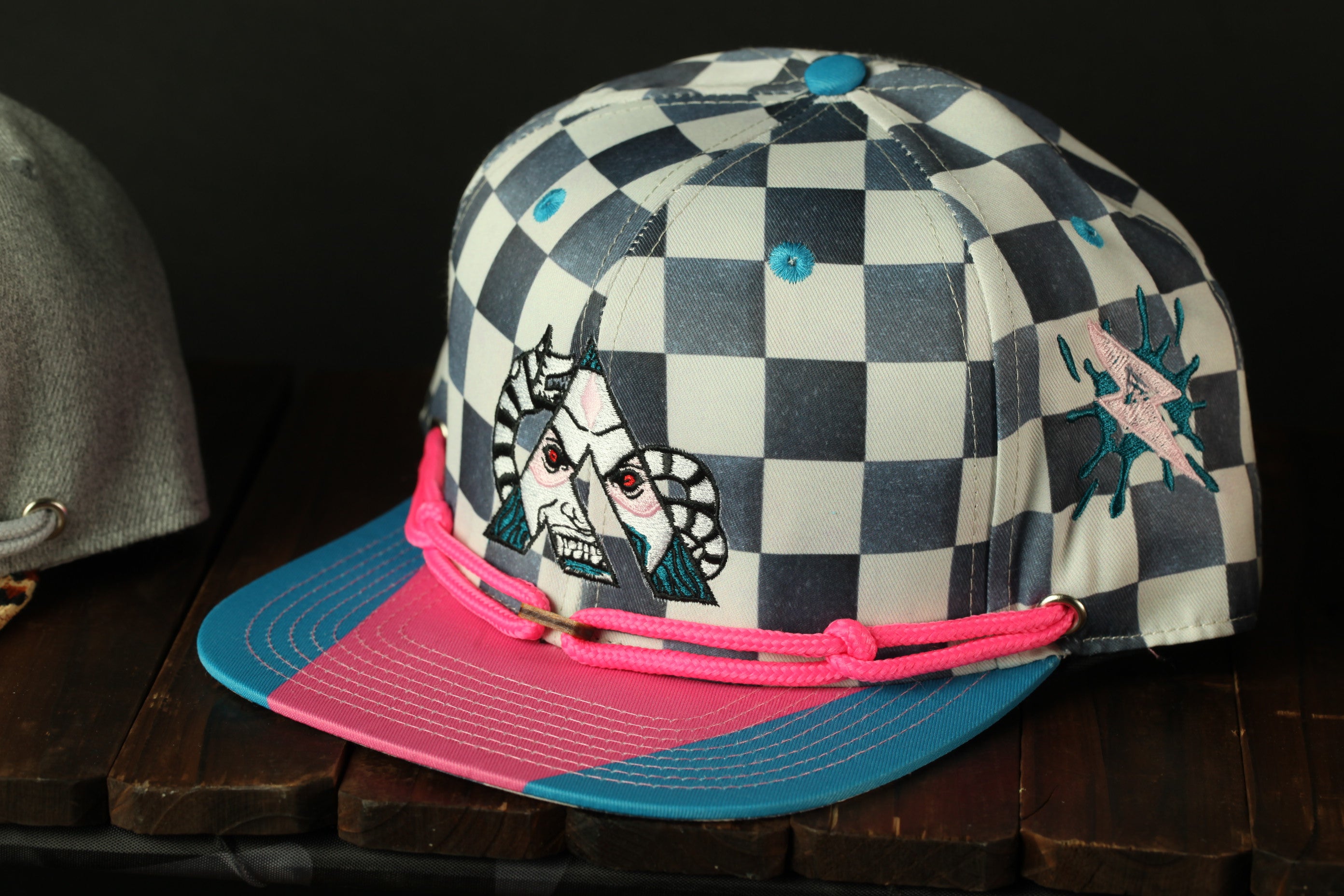 A colorful baseball cap with a checkered pattern and a graphic design on the front, sitting on a wooden surface.