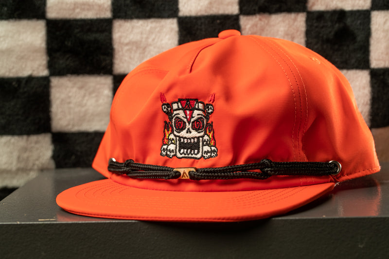 An orange baseball cap with a skull design on the front, sitting on a surface against a checkered background.