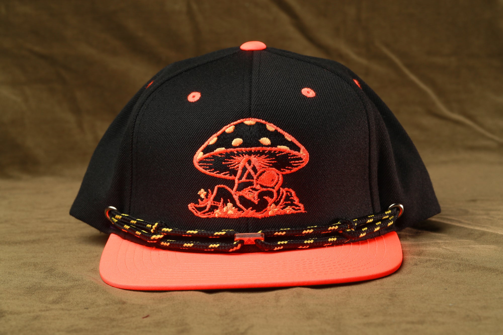 A black baseball cap with a red mushroom design and a black and orange lanyard.