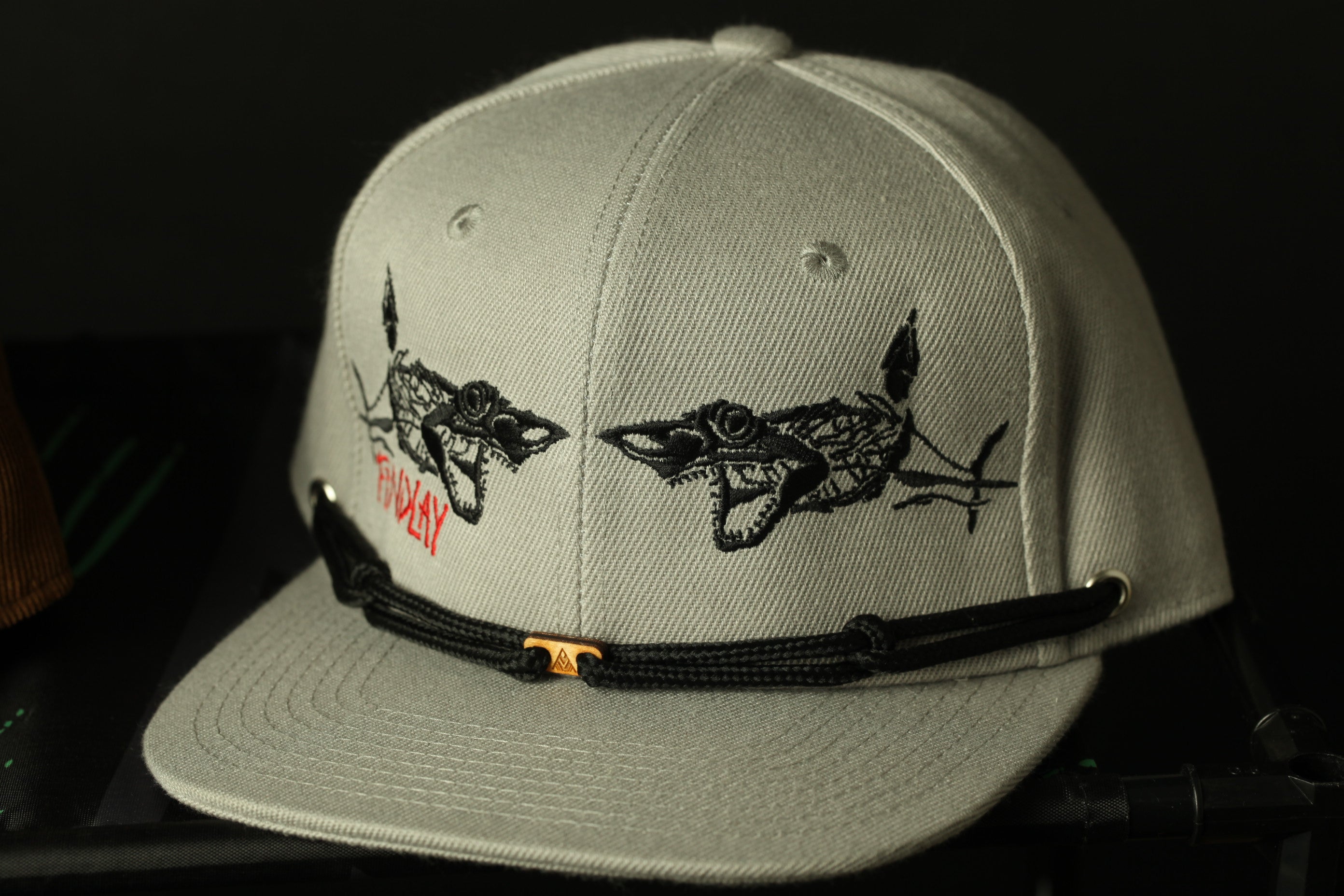 A gray baseball cap with a black graphic design on the front, featuring a shark or sea creature with a fierce expression.