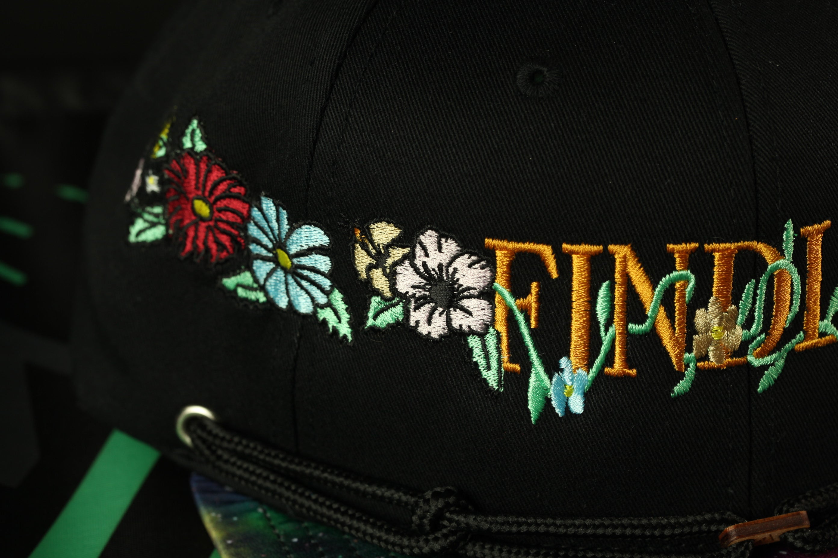 A close-up view of a black baseball cap with colorful floral embroidery on the front.