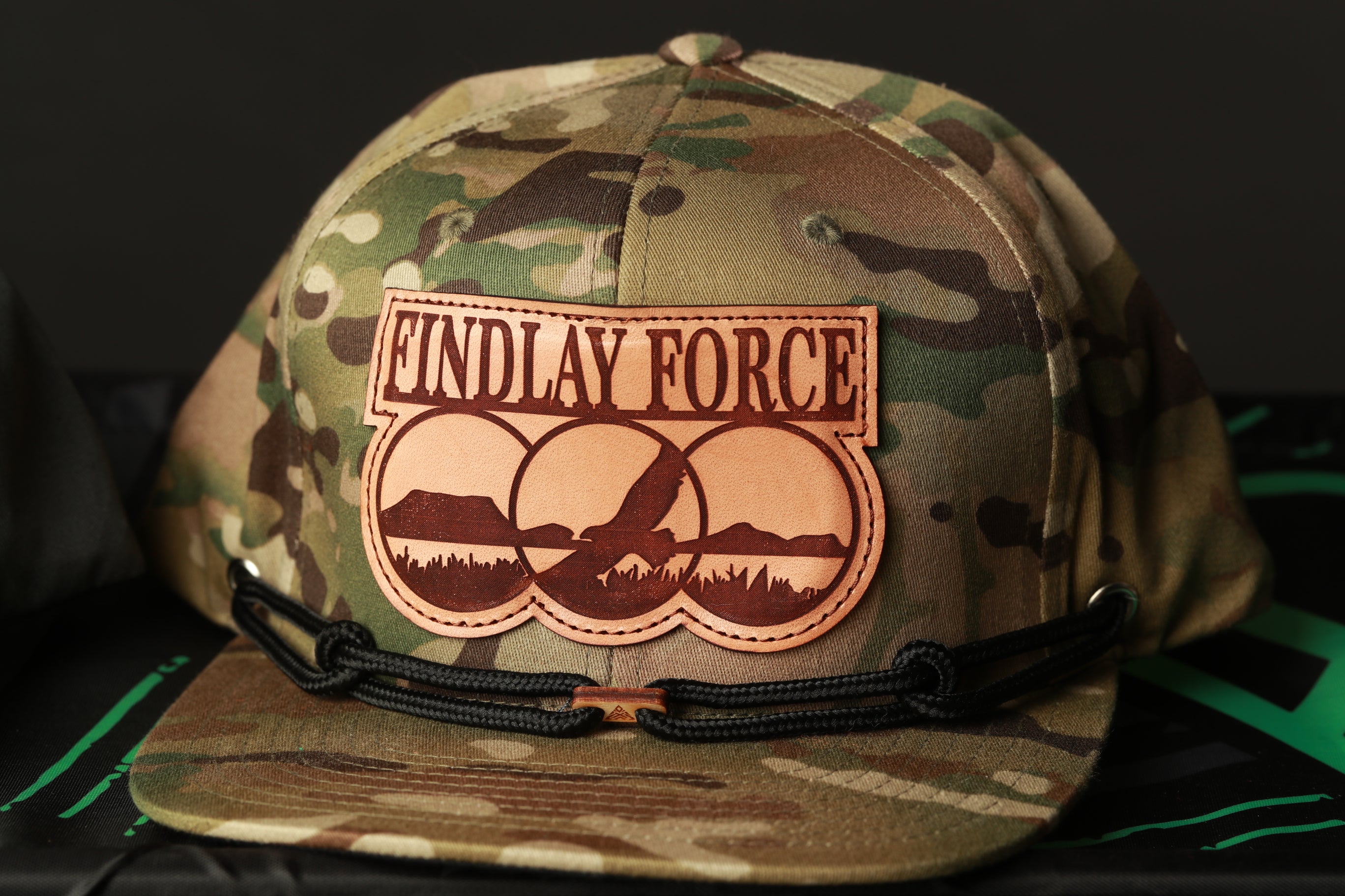 A camouflage baseball cap with a leather patch that says "ENDLAY FORCE" and a graphic of a mountain range.