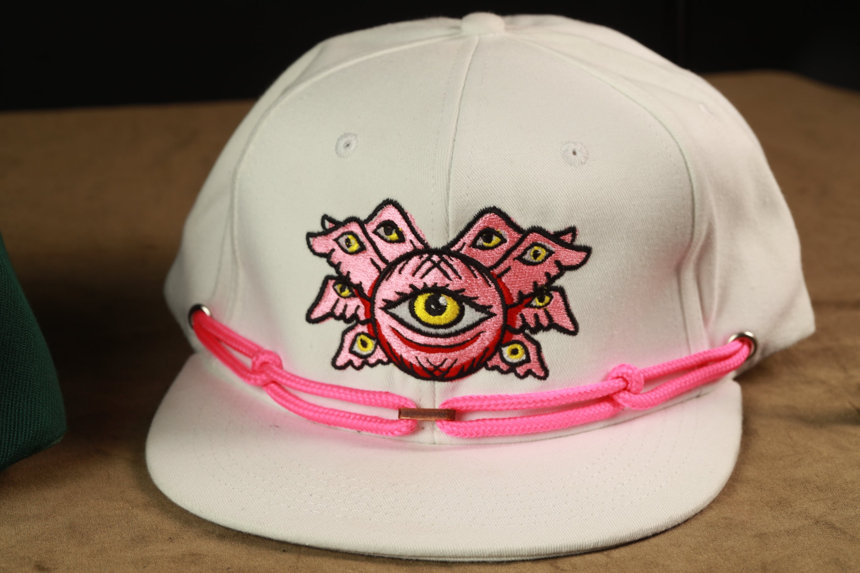 A white baseball cap with a pink and yellow embroidered design on the front.