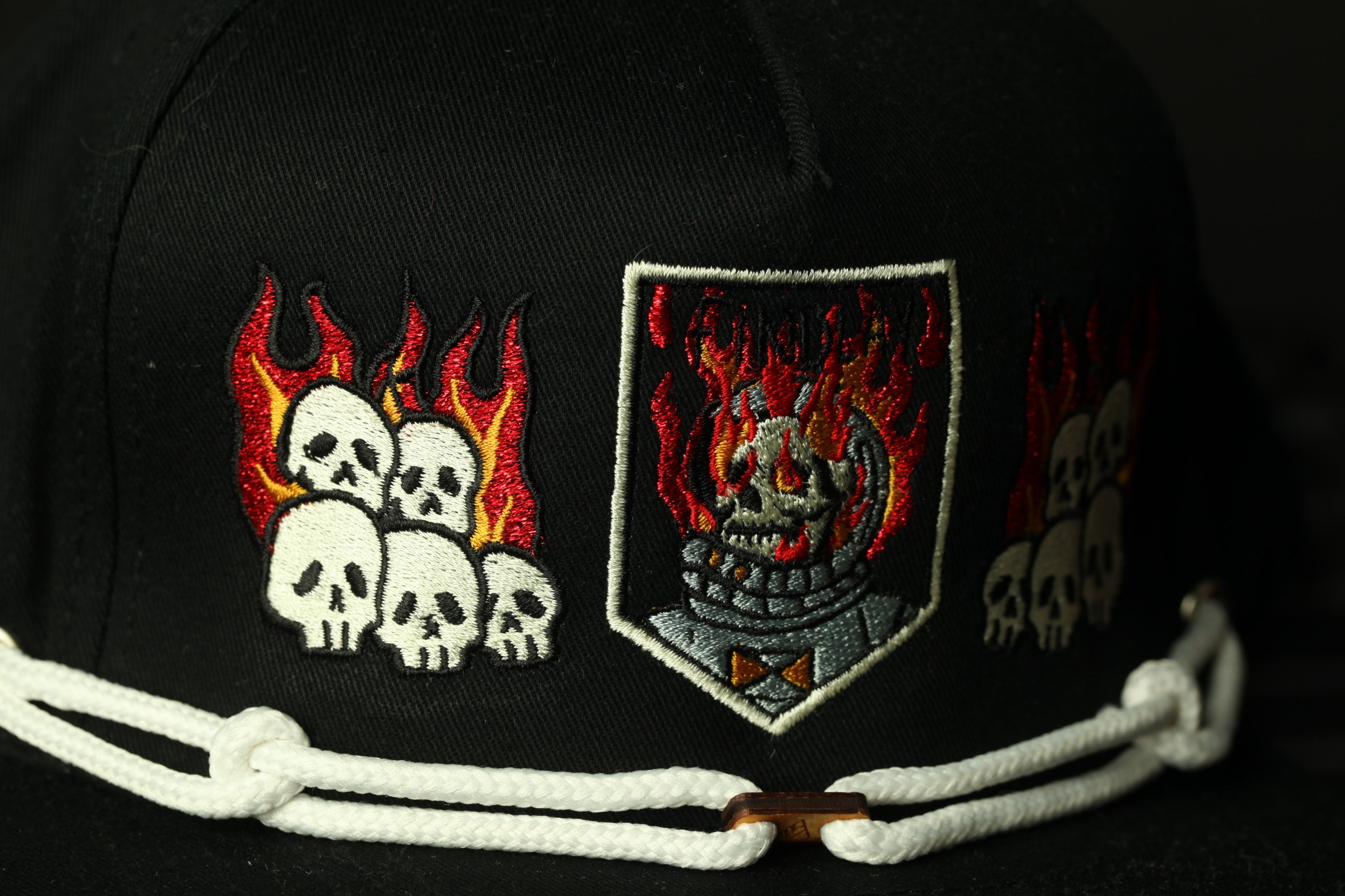 a close-up view of a black baseball cap with various embroidered designs, including flames, skulls, and a shield-shaped design.
