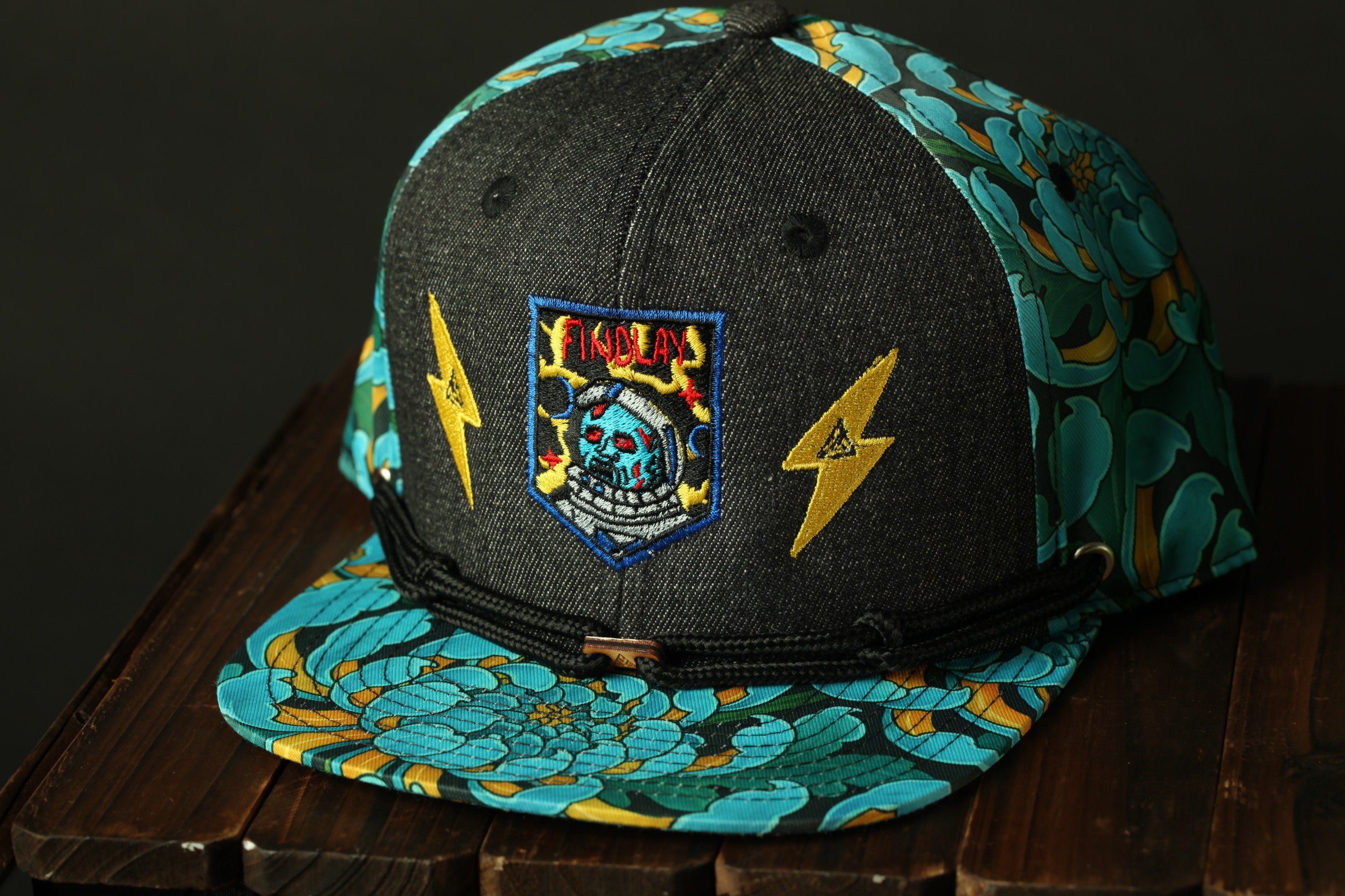 A colorful baseball cap with a floral pattern and a skull-like design on the front, sitting on a wooden surface.