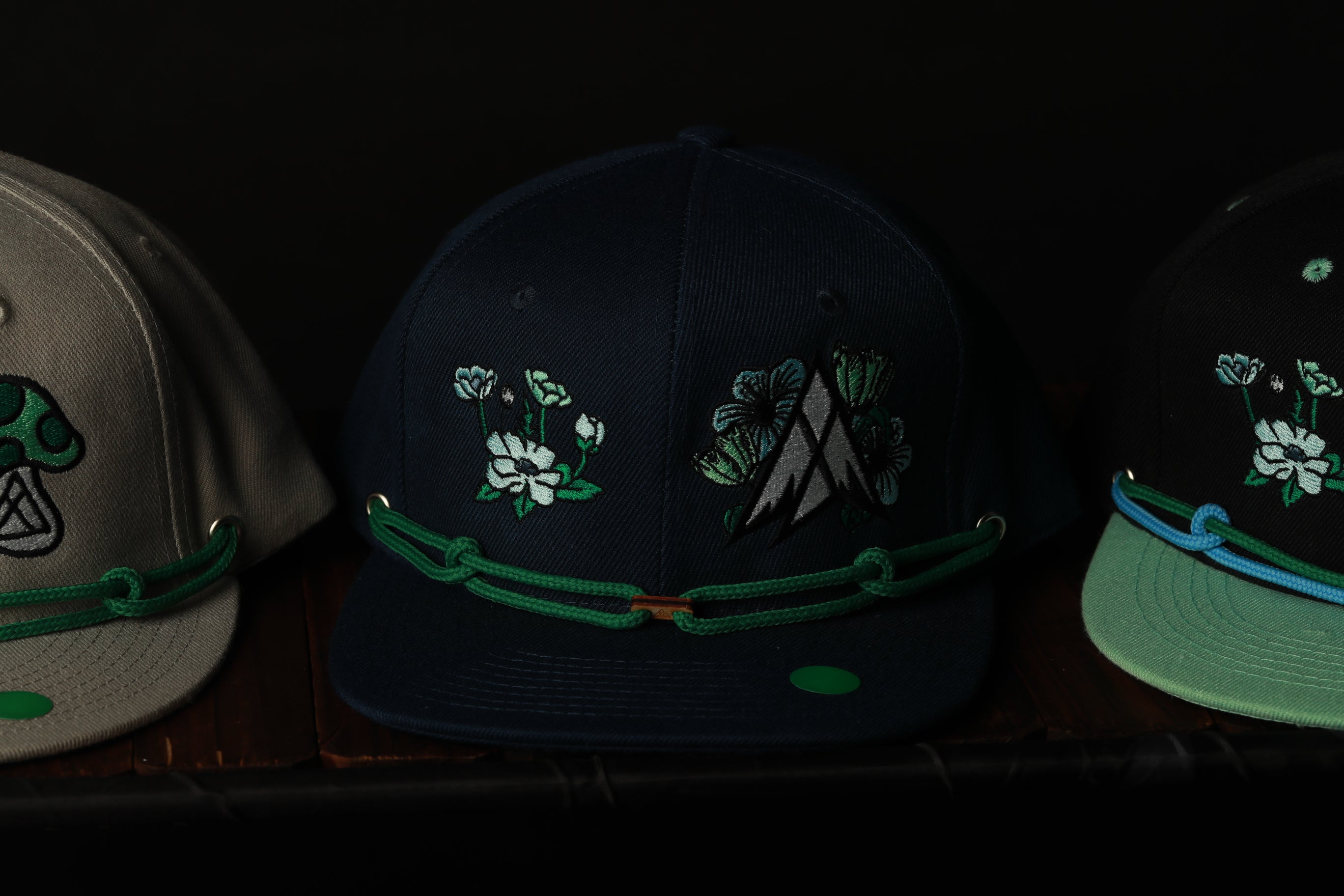 Three baseball caps with floral embroidery and green straps are displayed on a shelf.