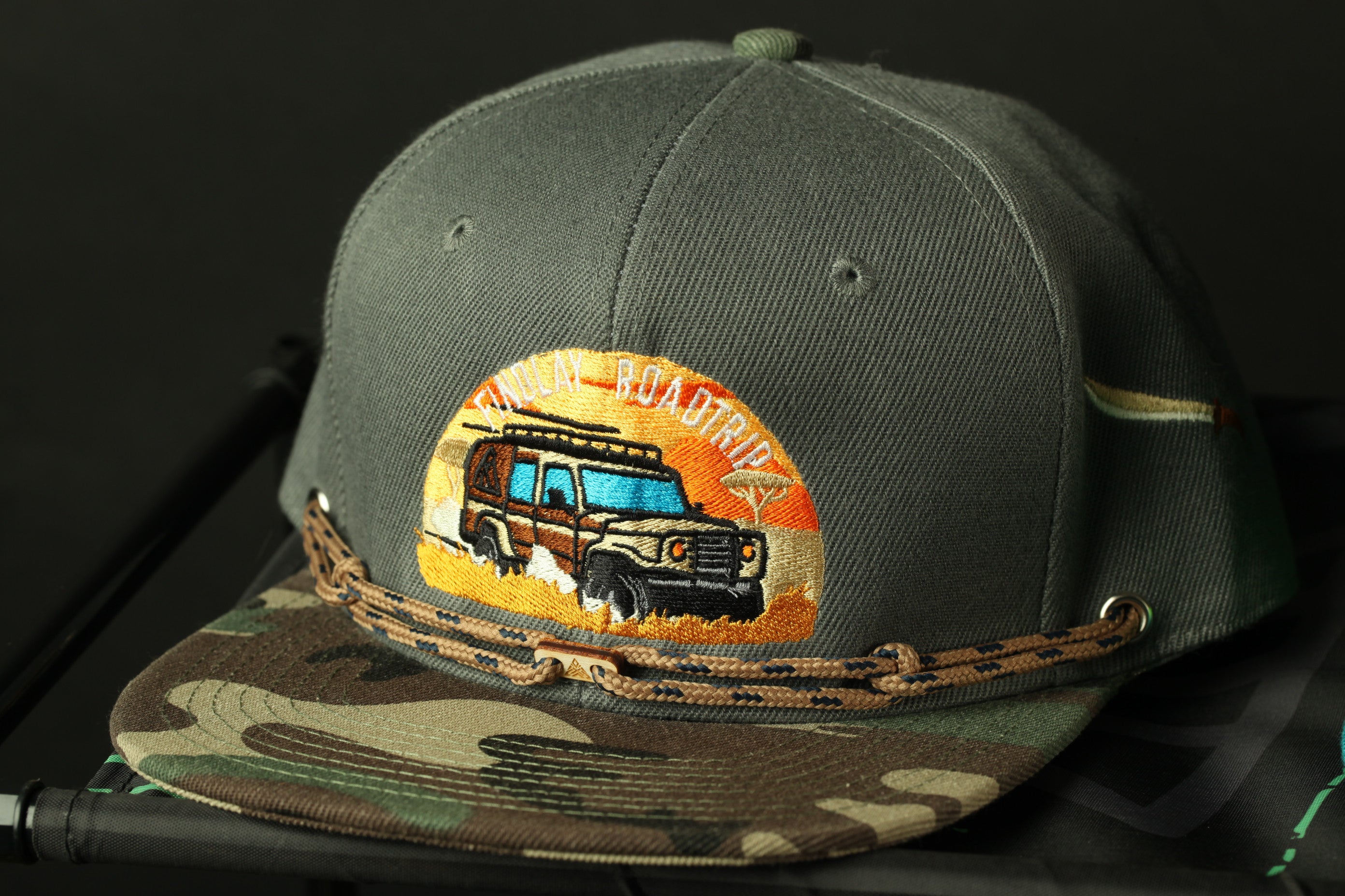 A gray baseball cap with a camouflage pattern and an embroidered patch on the front, featuring a truck design.