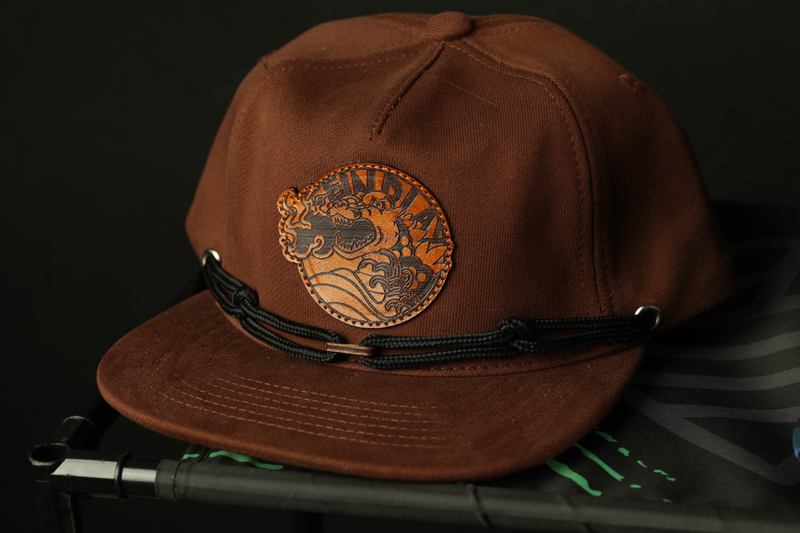 A brown baseball cap with a circular logo on the front, sitting on a black surface.