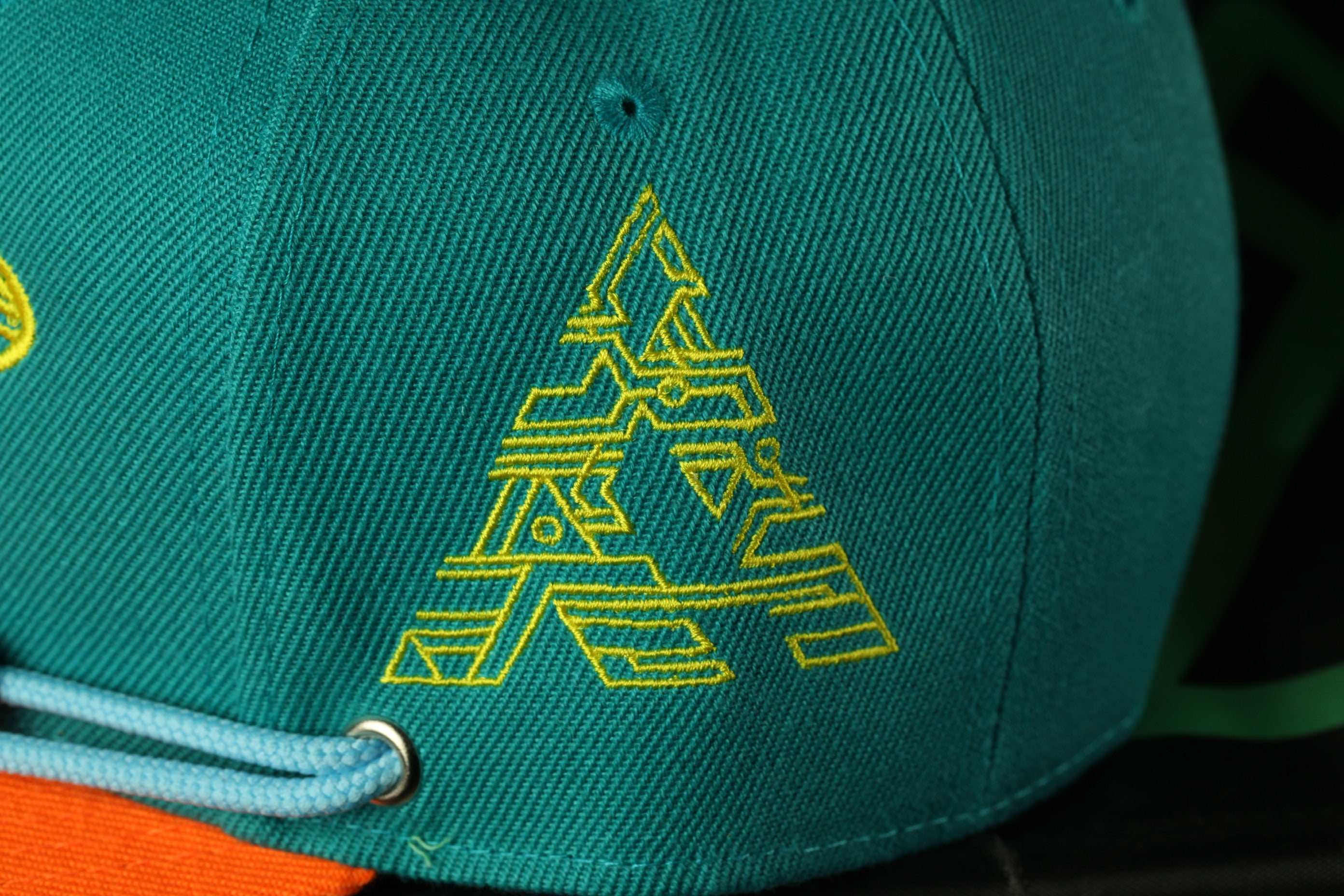 A close-up view of a green baseball cap with a yellow geometric design on the front.