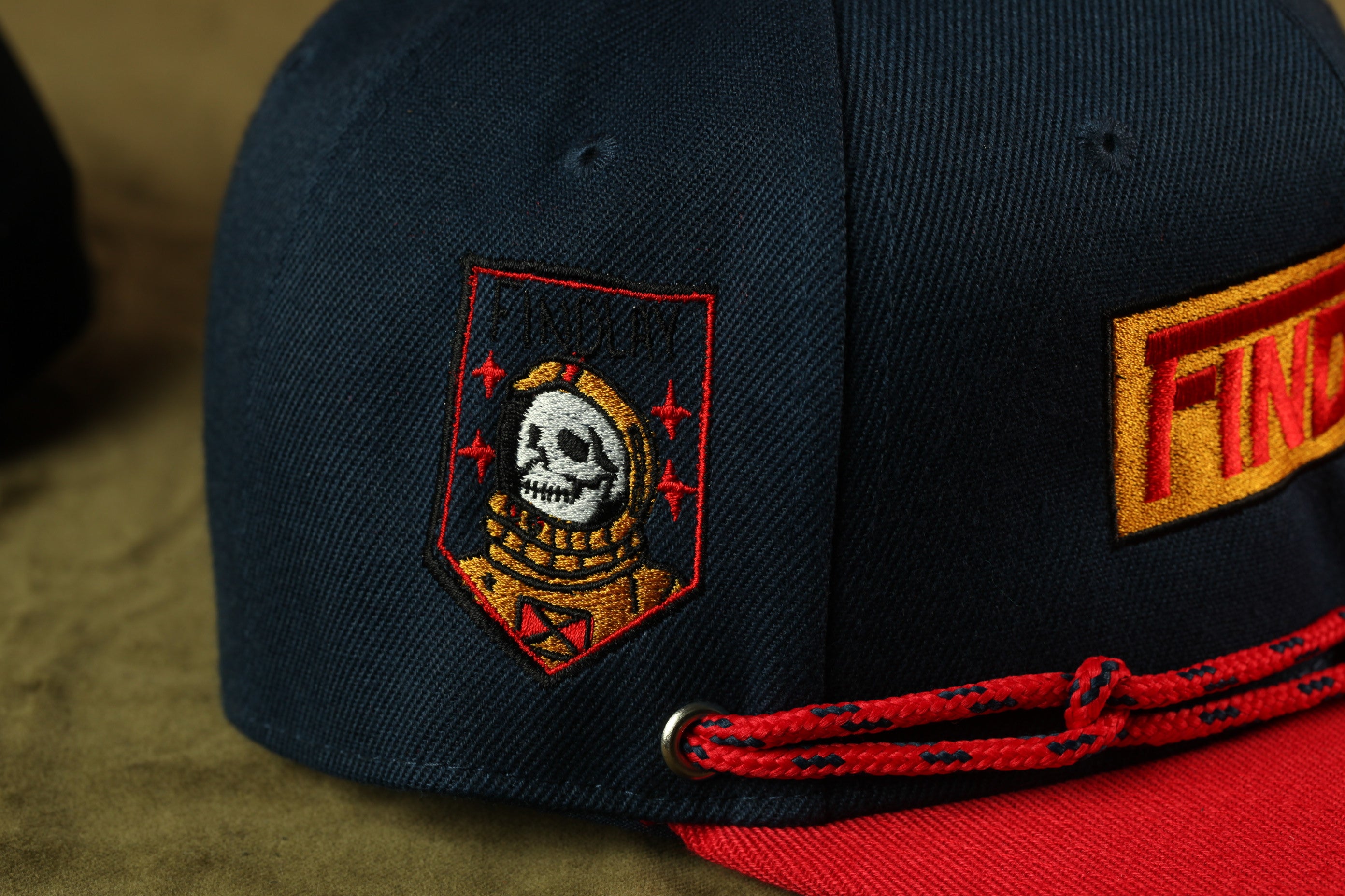 A close-up view of a dark blue baseball cap with a red and yellow patch featuring a skull and crossbones design.