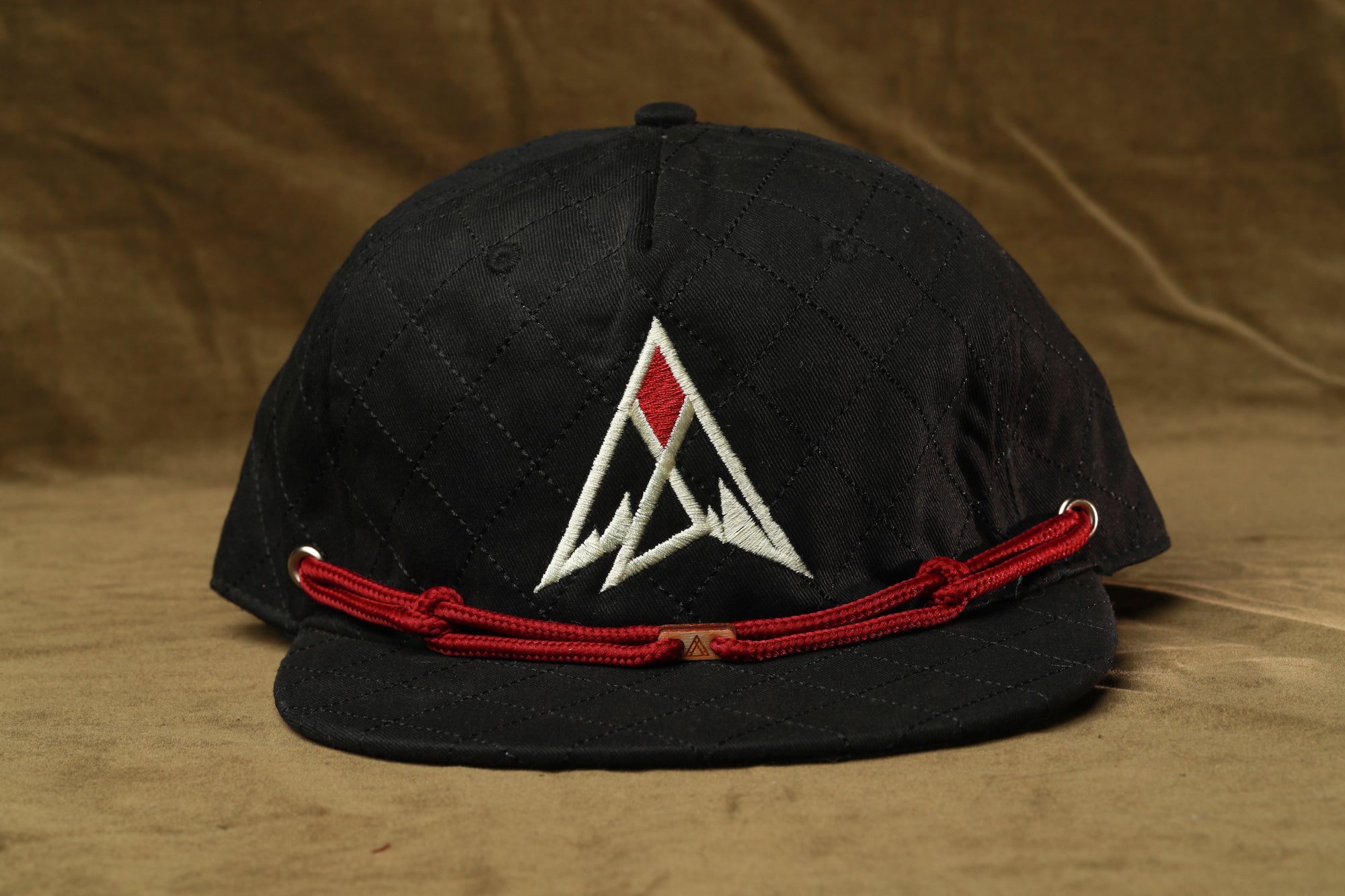A black baseball cap with a red string and a white logo on the front.