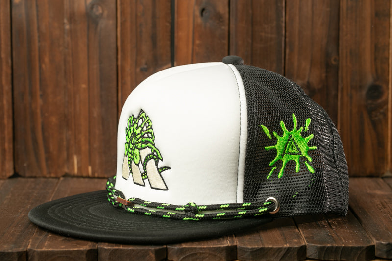 A white and black baseball cap with a green and black design on the side, sitting on a wooden surface.