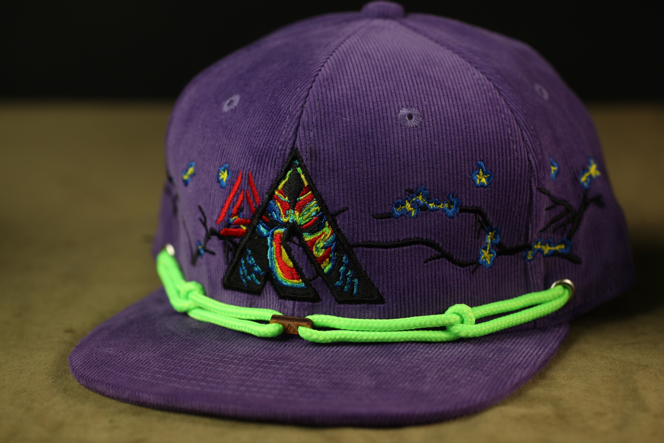 A purple baseball cap with a colorful, embroidered design on the front.