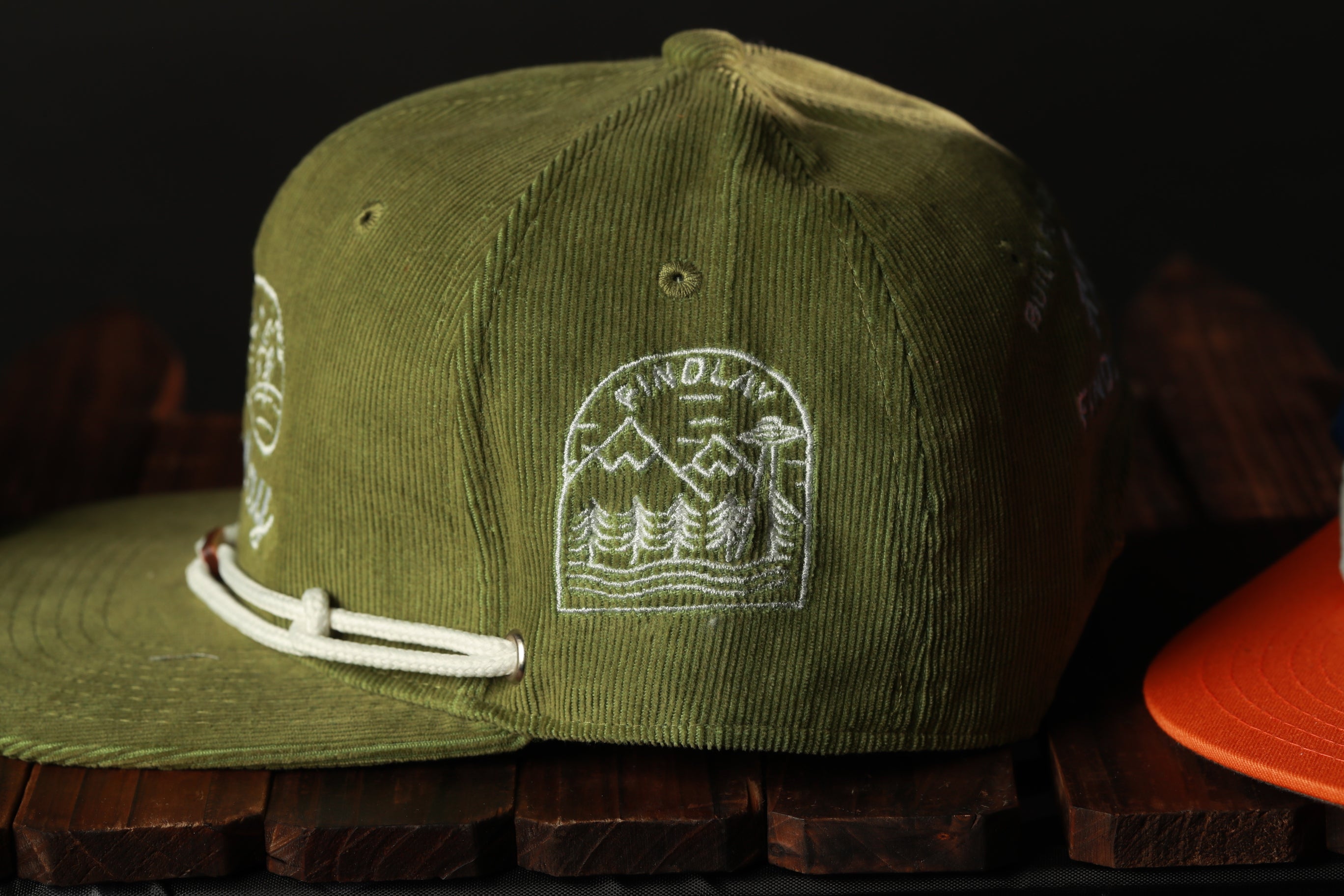 A green baseball cap with a white embroidered design on the front, resting on a wooden surface.