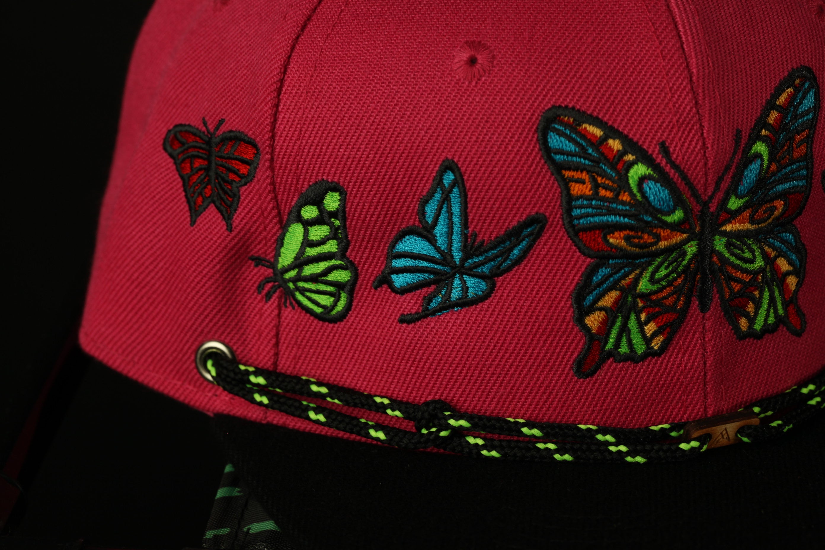 A close-up view of a red baseball cap with colorful butterfly embroidery on the front.
